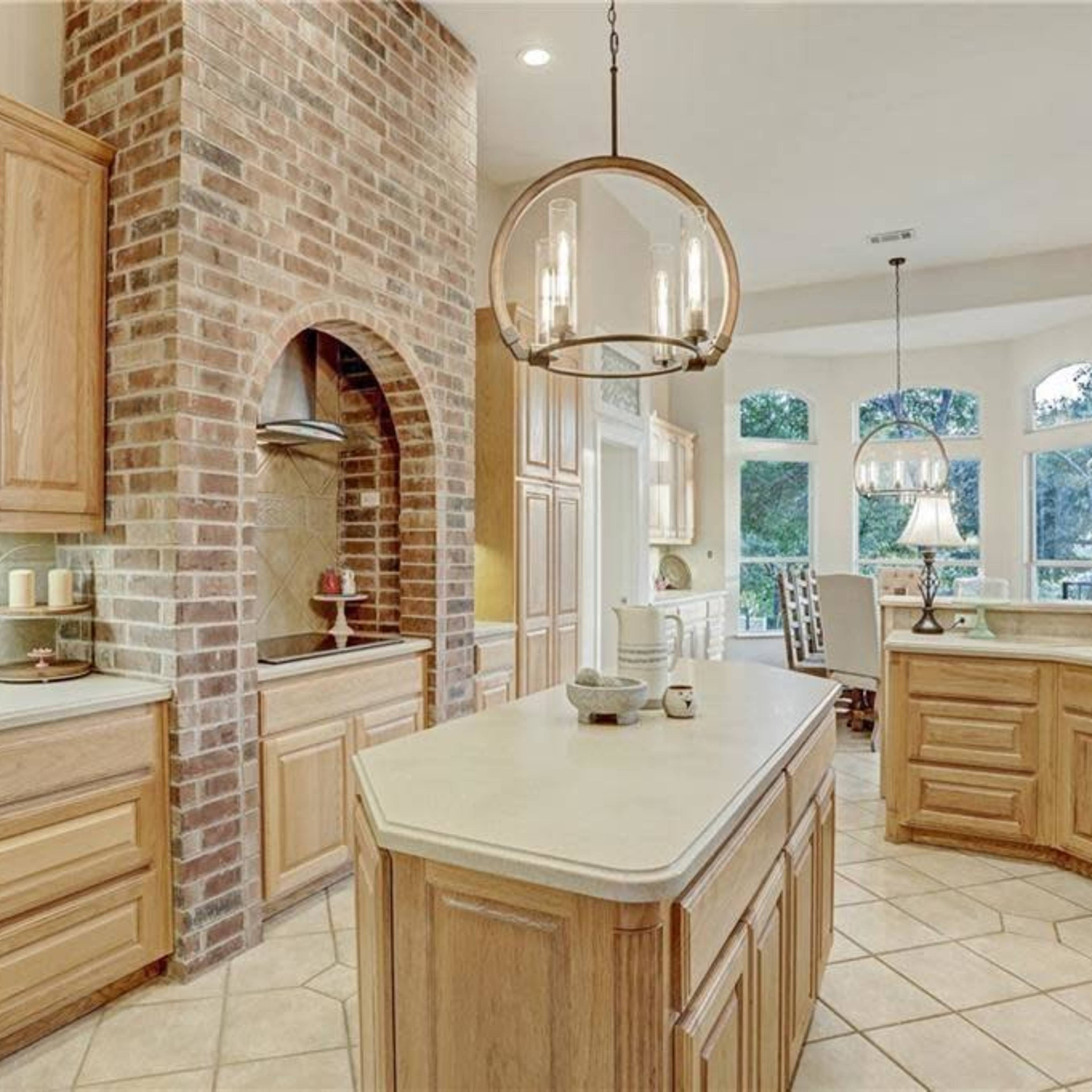 A spacious kitchen features wooden cabinets, a brick accent wall, and large windows that provide ample natural light.
