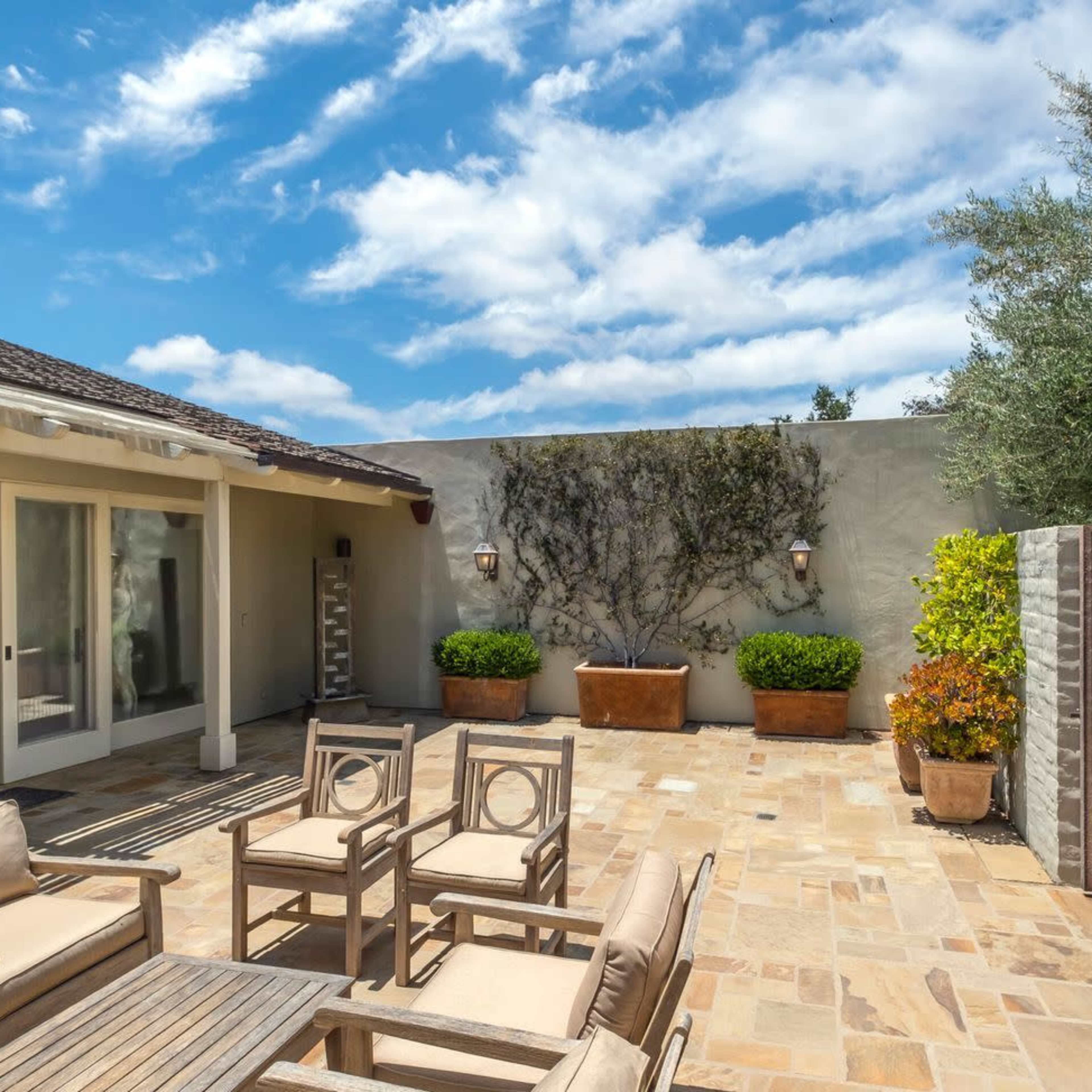 A stone patio with outdoor seating, surrounded by potted plants and a rustic wooden door.
