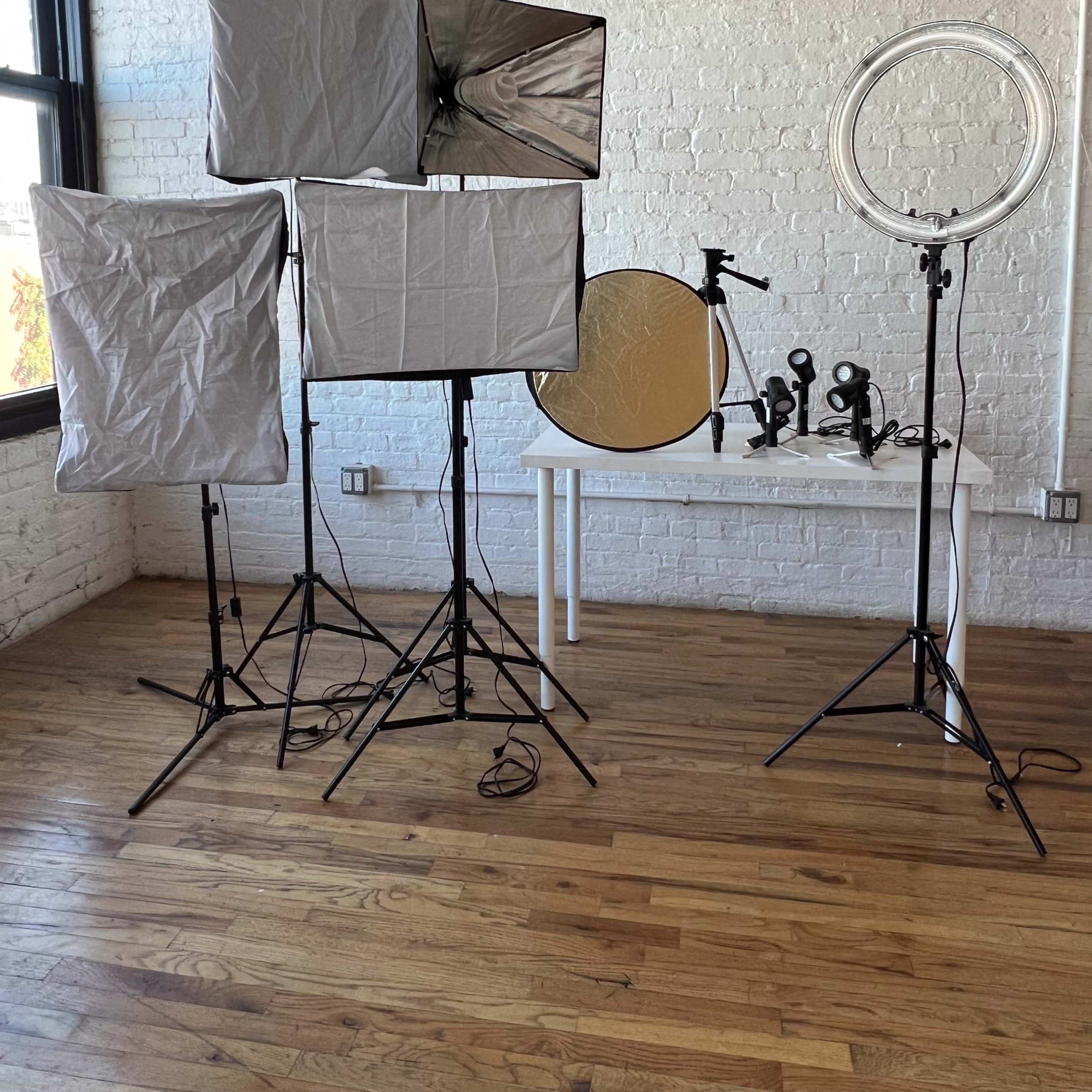 A photography setup in a room with large windows, featuring multiple lighting equipment and reflectors on stands arranged on a wooden floor.