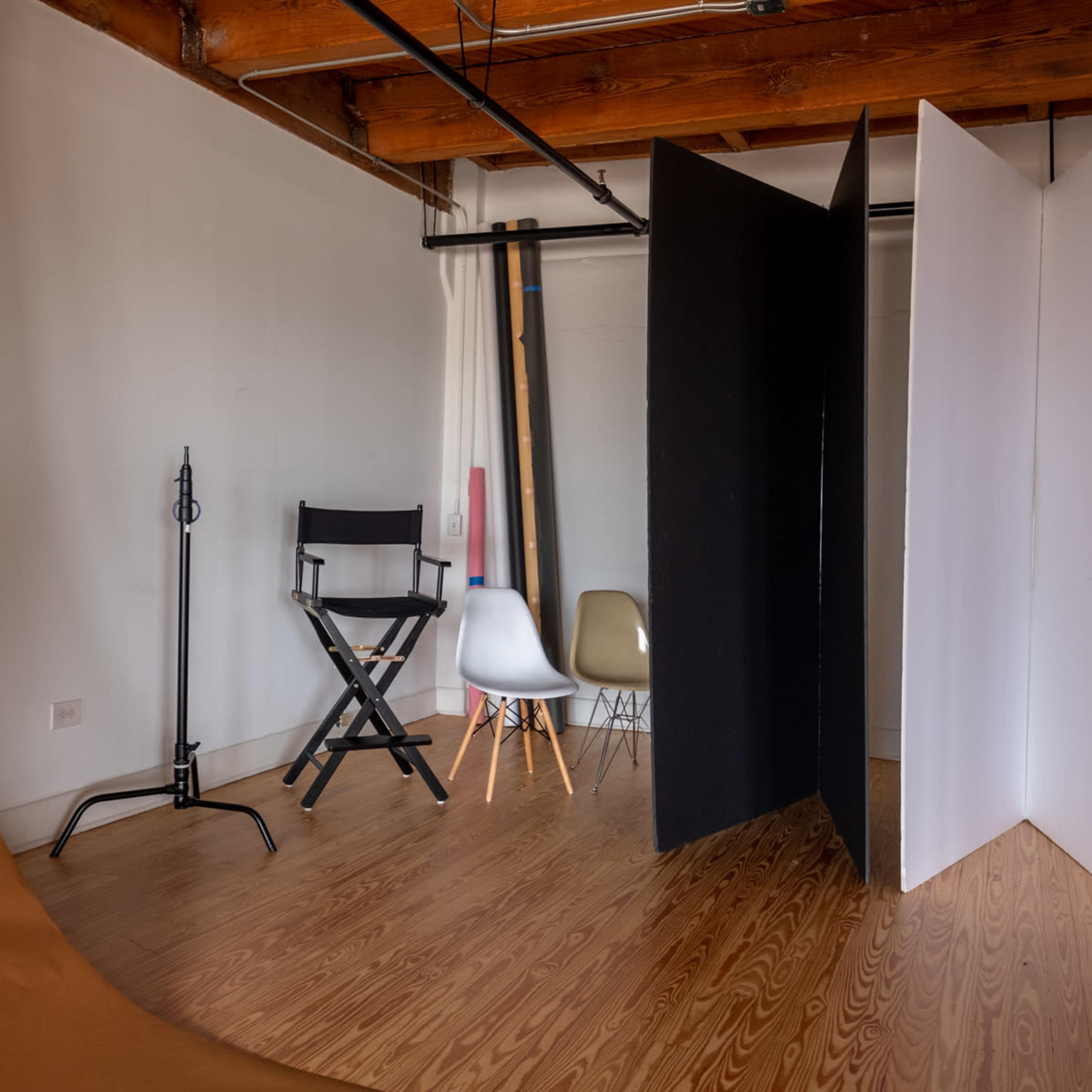 A photography studio with wooden floors, a director's chair, a collapsible backdrop, and two partition screens in black and white.