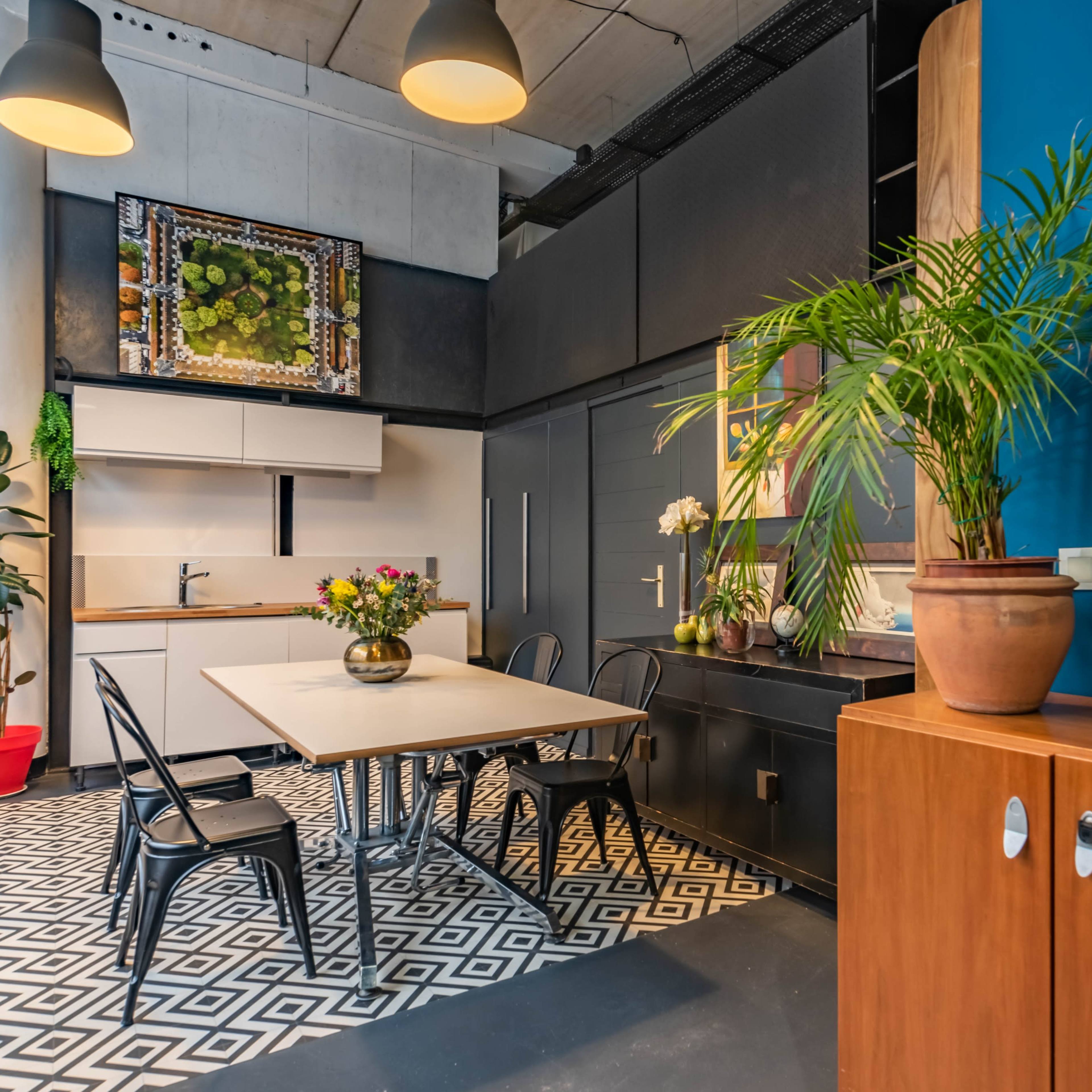 A modern kitchen and dining area featuring a table with chairs, a wall-mounted artwork, and a potted plant beside a wooden cabinet.