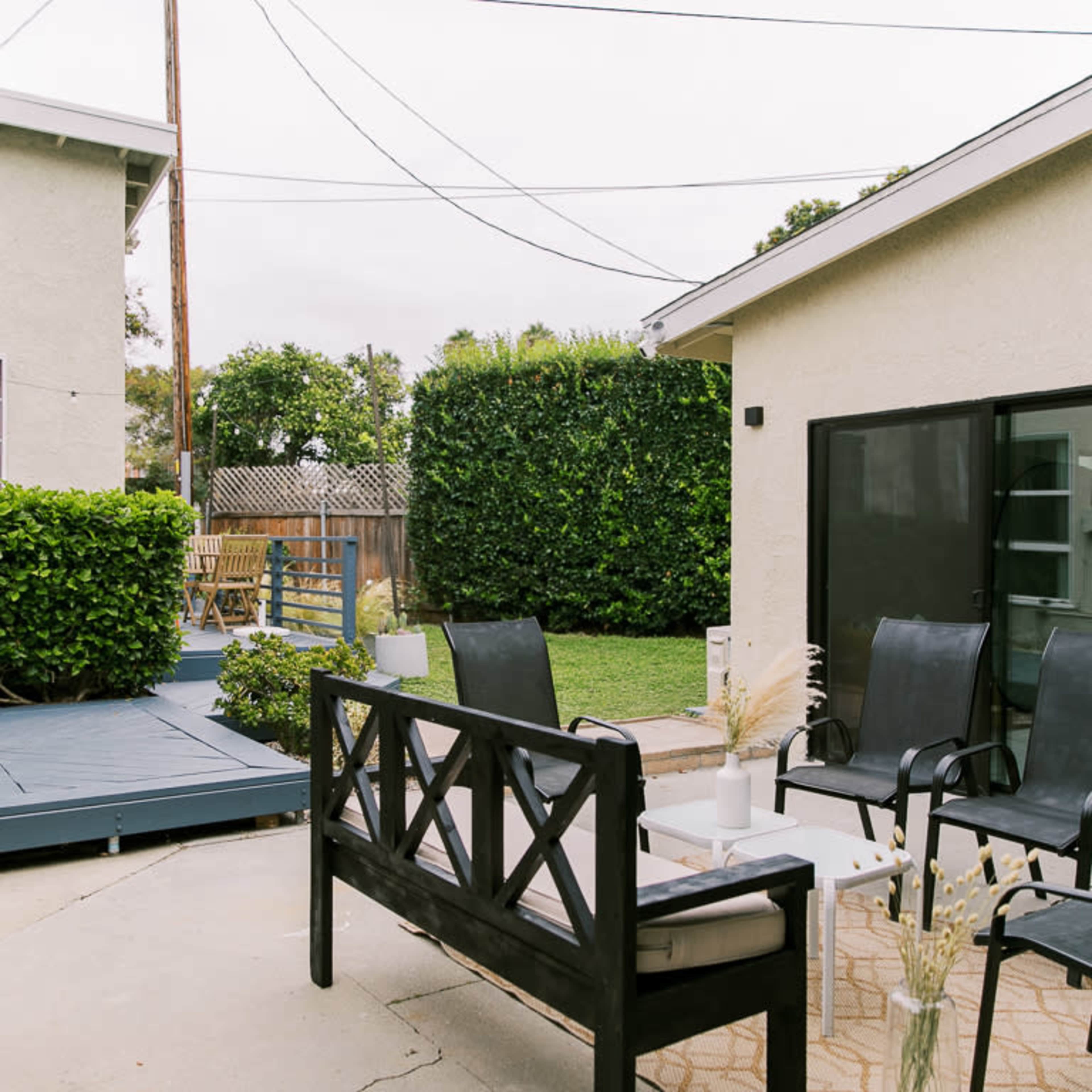 A backyard area with seating, a small table, and a deck surrounded by greenery.