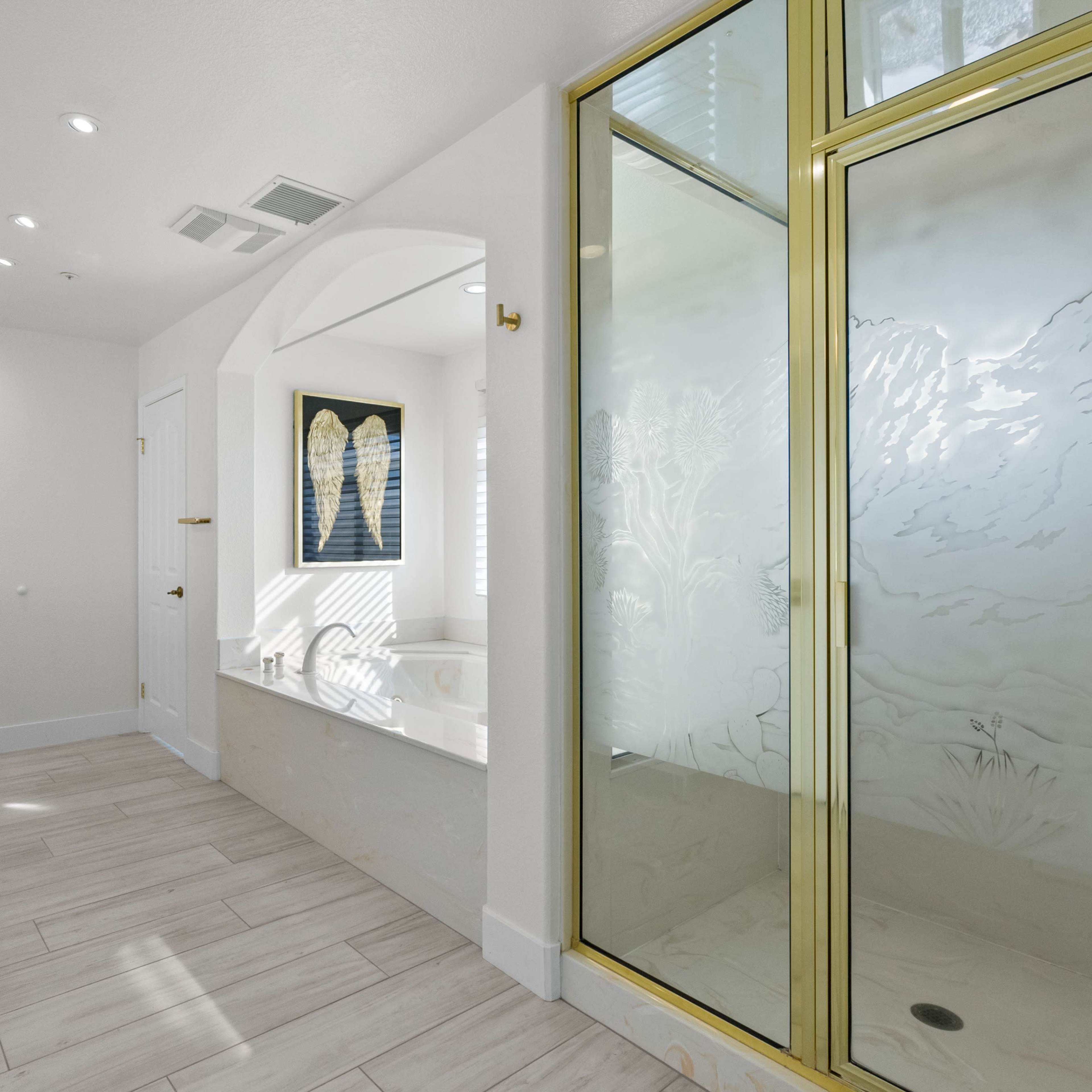 A modern bathroom featuring a glass shower with gold trim, a tub beside it, and two sinks illuminated by decorative light fixtures.