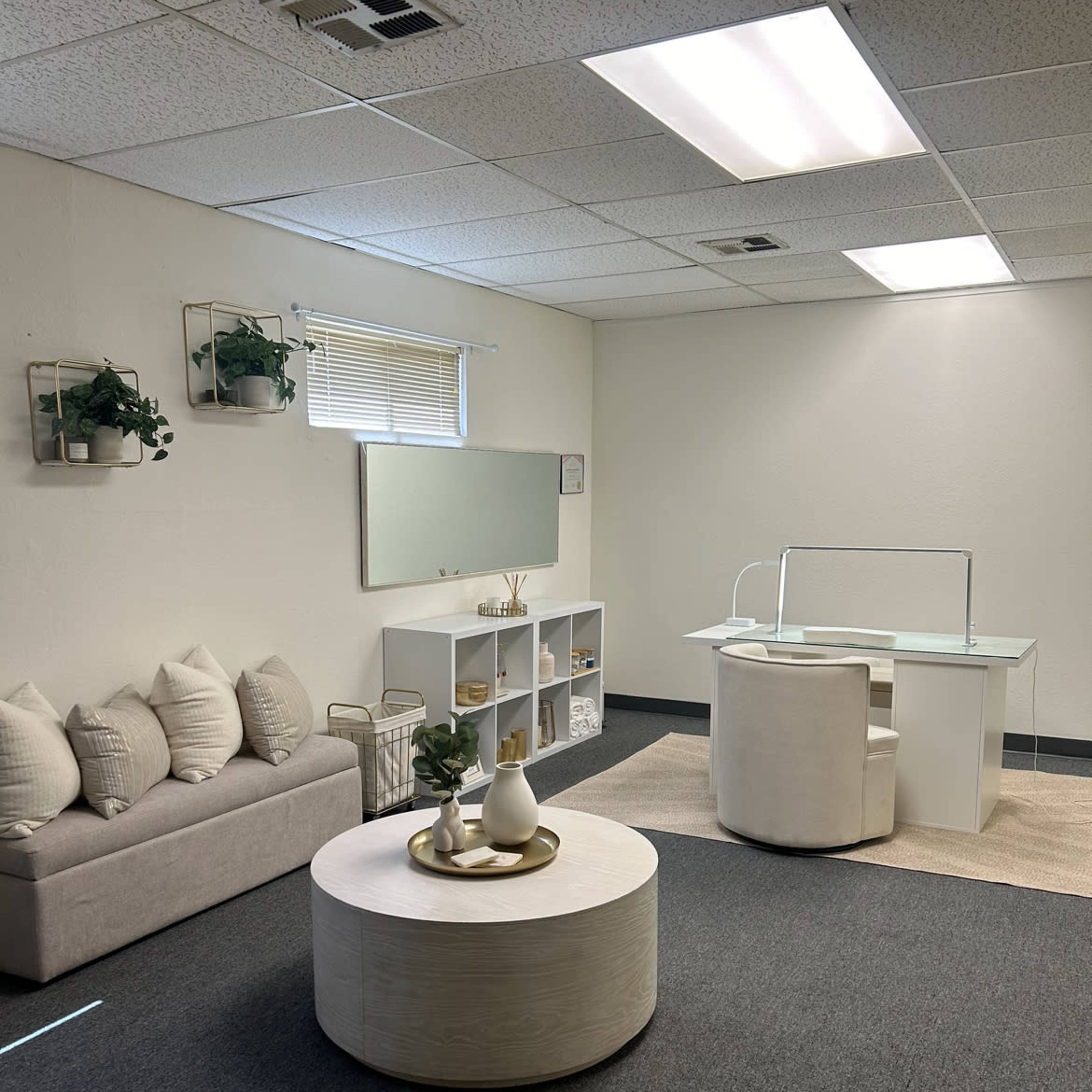 A minimalistic office space with a light-colored desk and chair, a round coffee table, and decorative plants against a neutral wall.