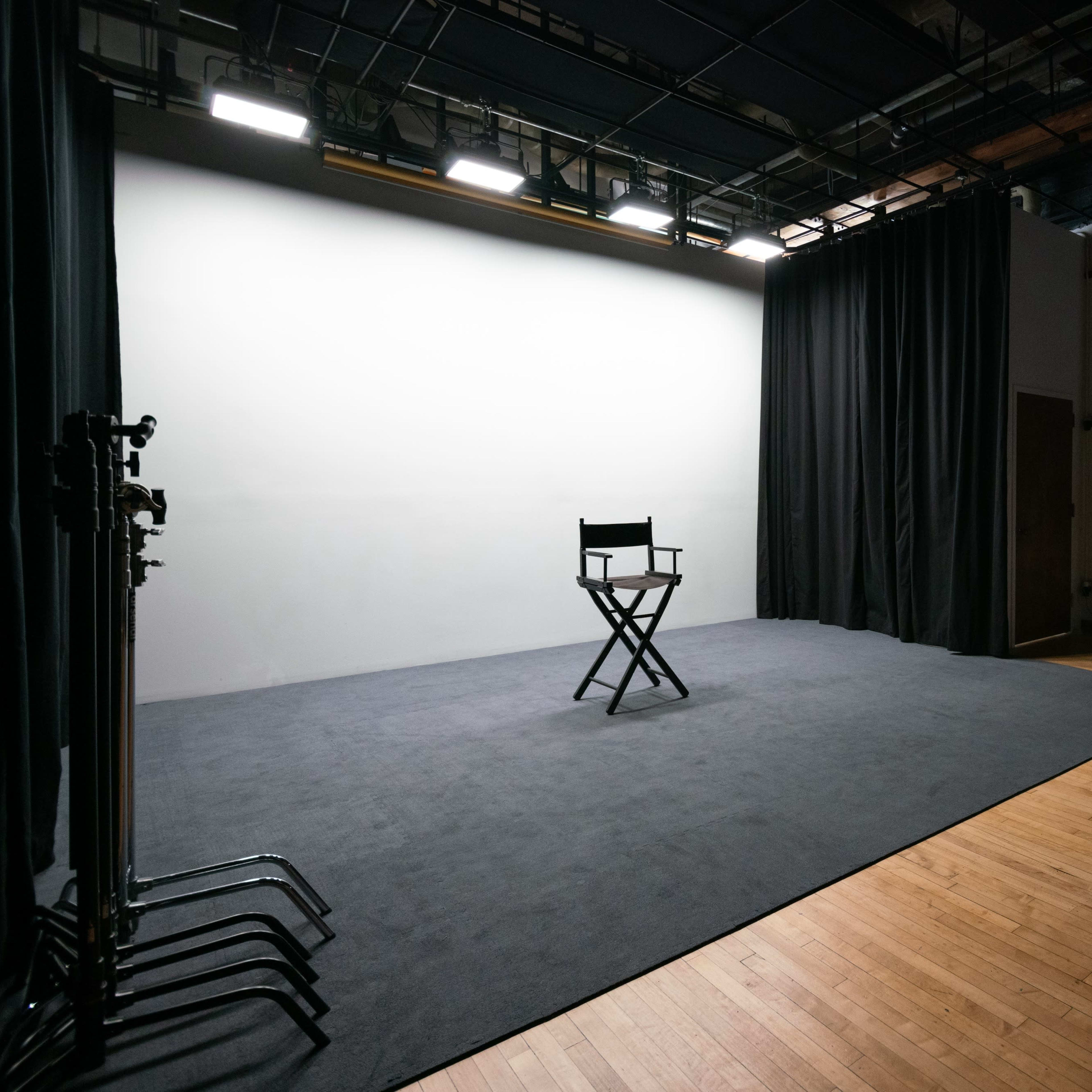 A spacious, empty studio with a single director's chair facing a blank wall, surrounded by black curtains and dim lighting.