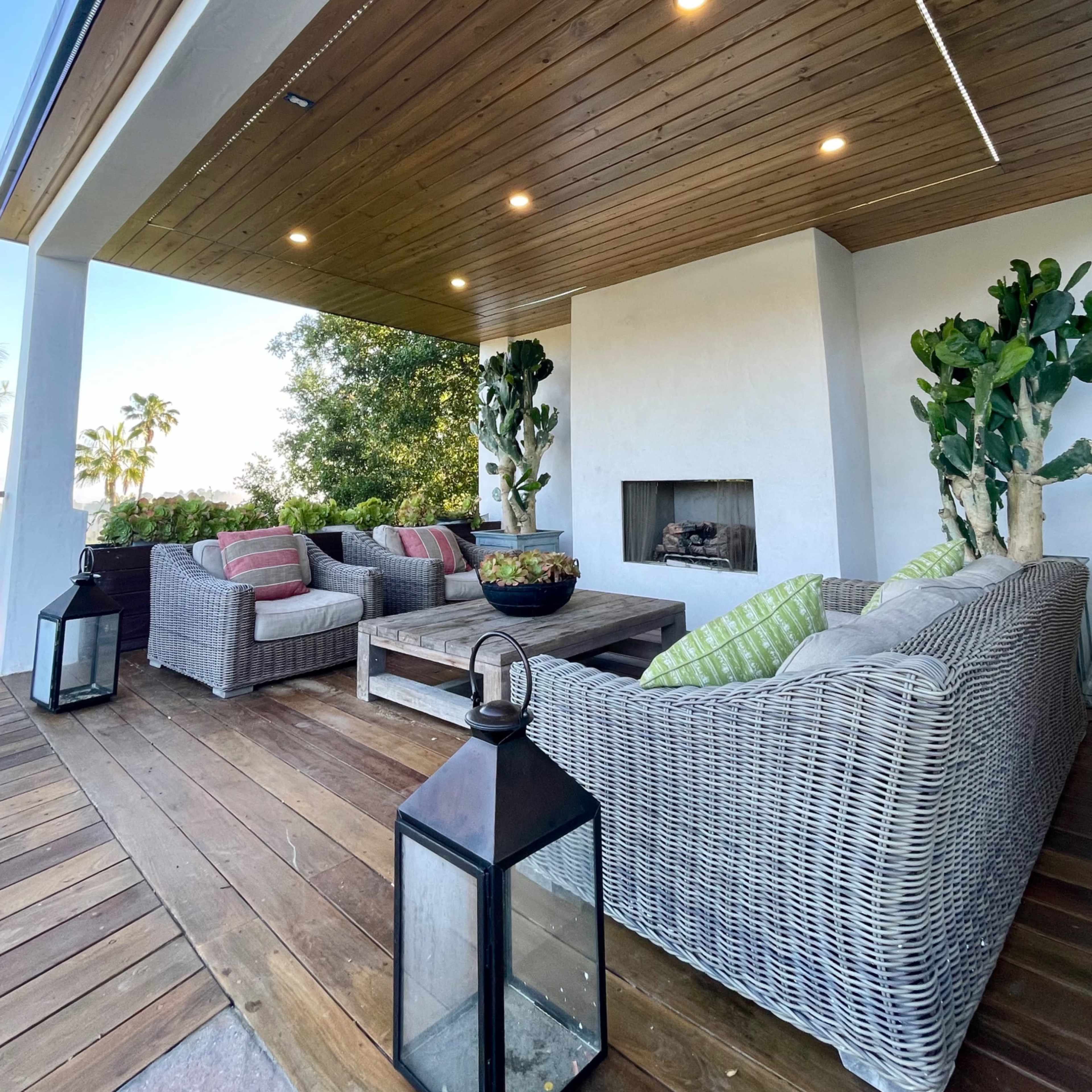 A covered outdoor seating area features wicker furniture, a coffee table, and decorative plants.