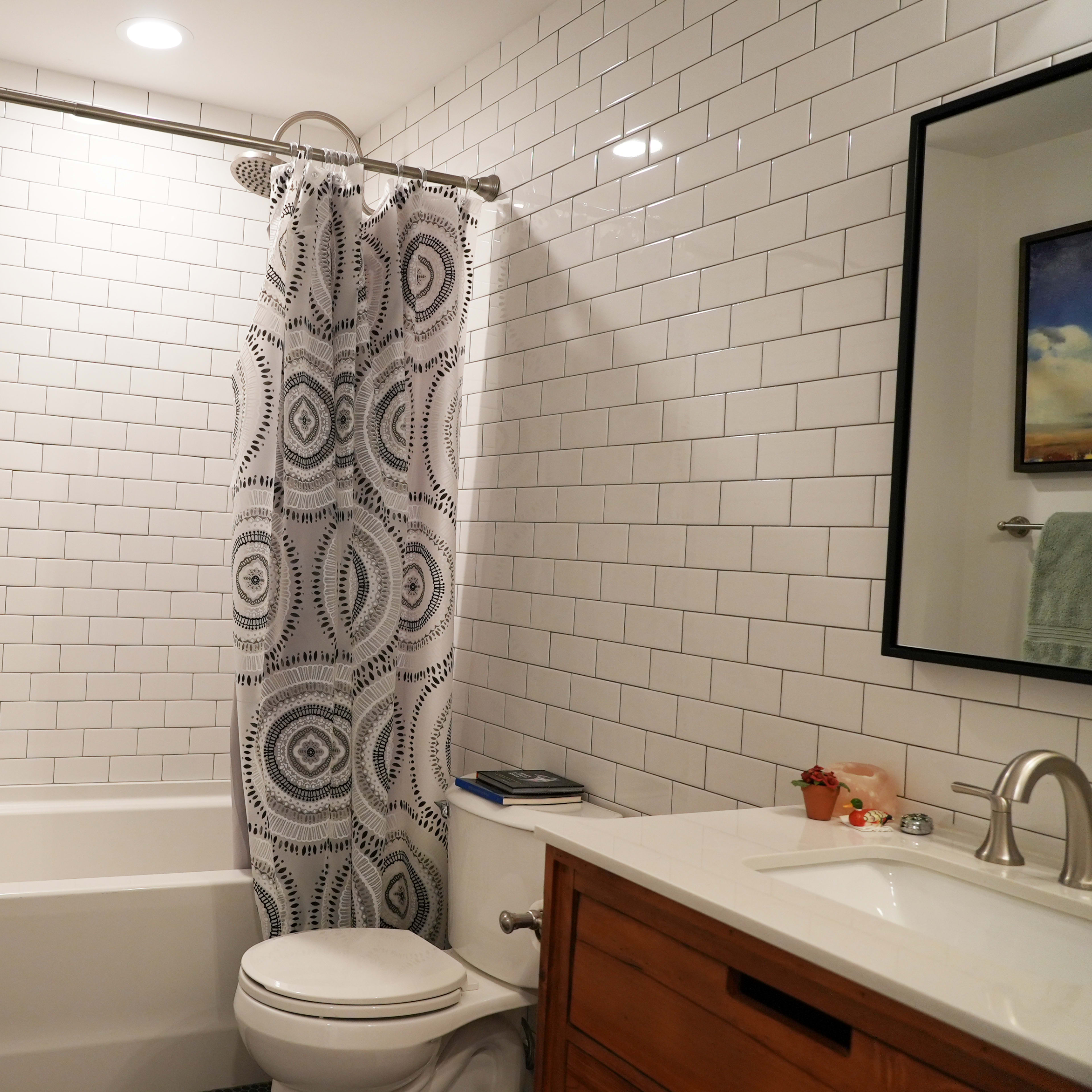 A bathroom with a bathtub, shower curtain, white tiled walls, and a wooden vanity with a sink.