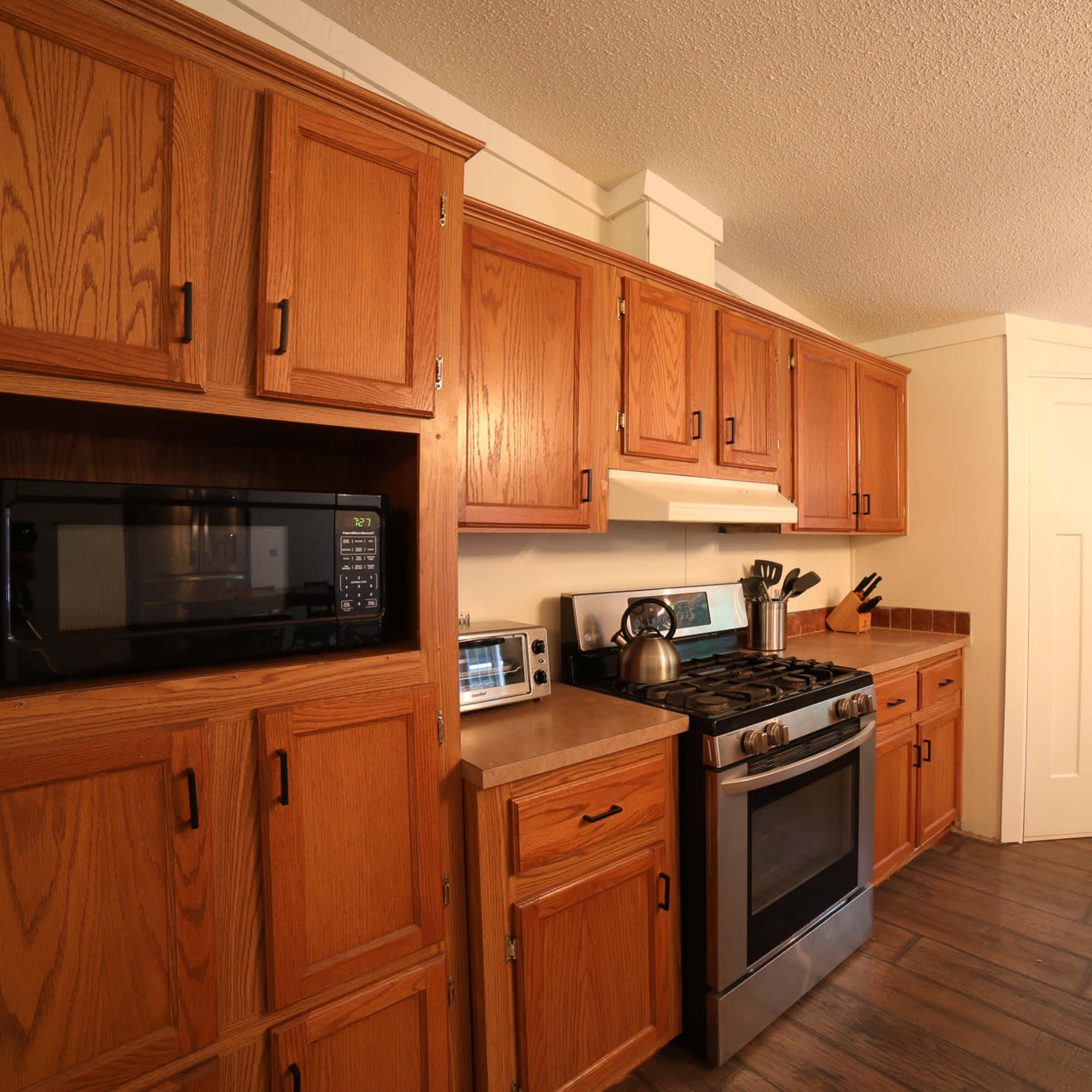 A kitchen with wooden cabinets, a stainless steel stove, a microwave, and a window letting in natural light.