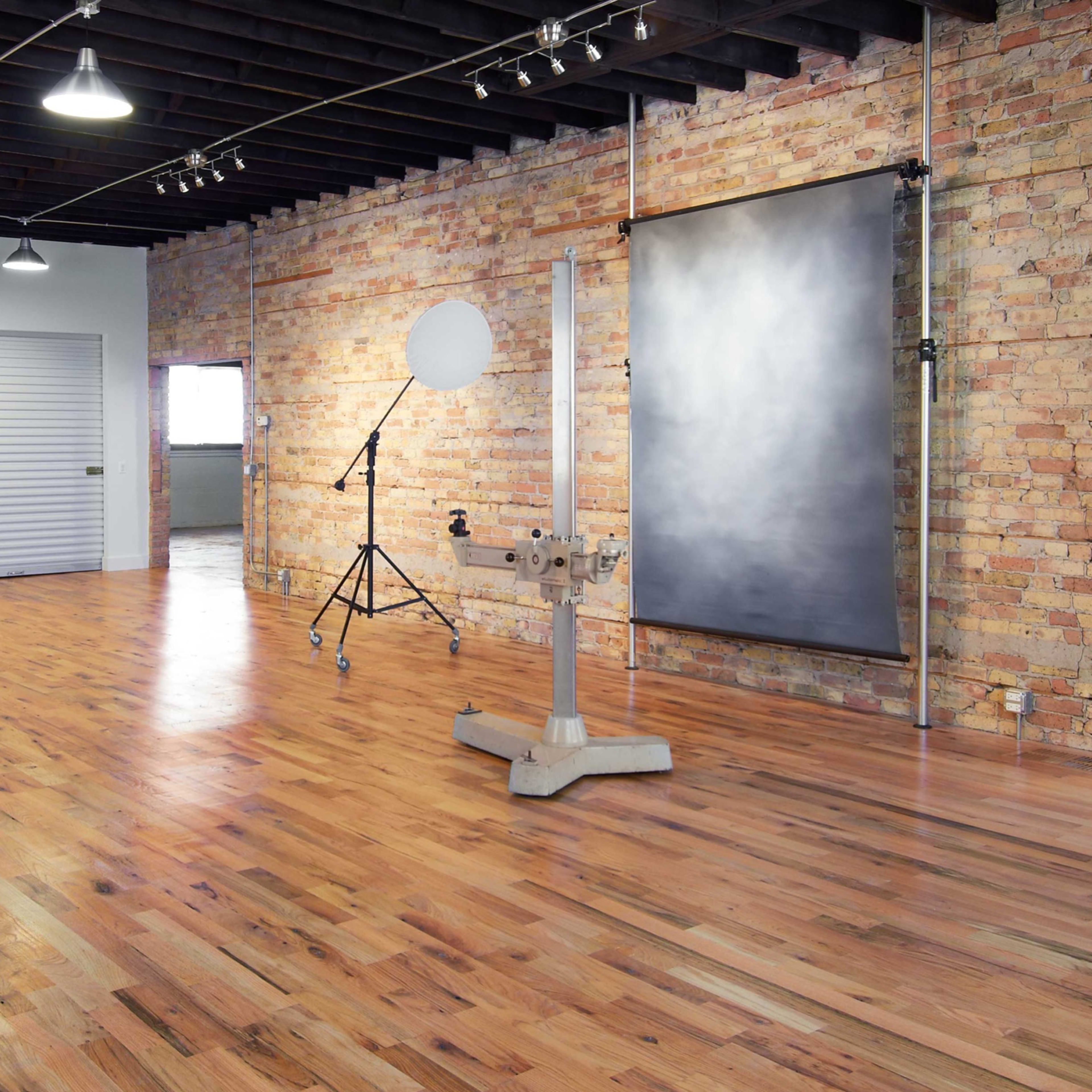 A spacious, well-lit room with wooden floors, exposed brick walls, and several doors leading to other areas.