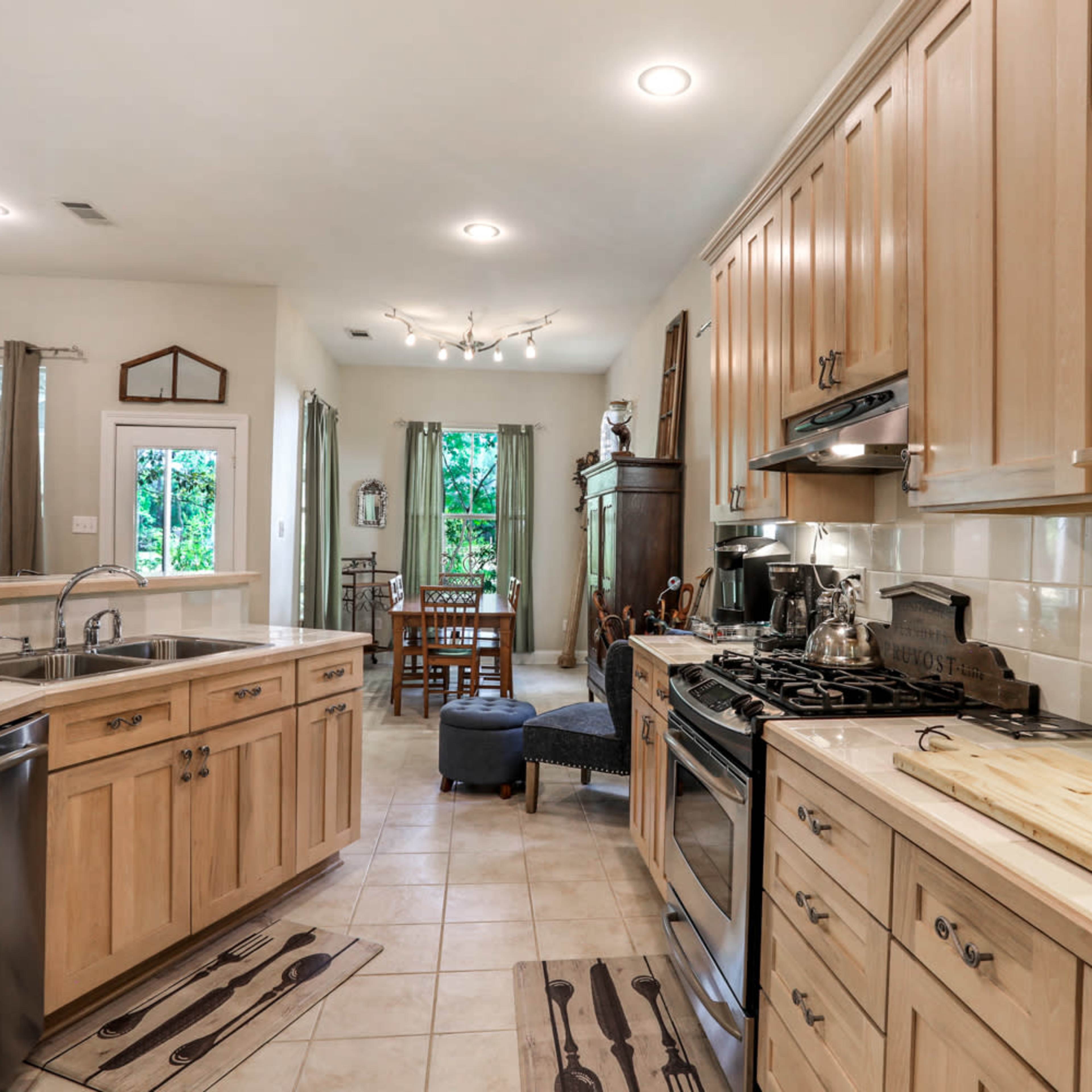 A modern kitchen with wooden cabinetry, a stainless steel dishwasher, and a gas stove, leading into a dining area with a wooden table and chairs.
