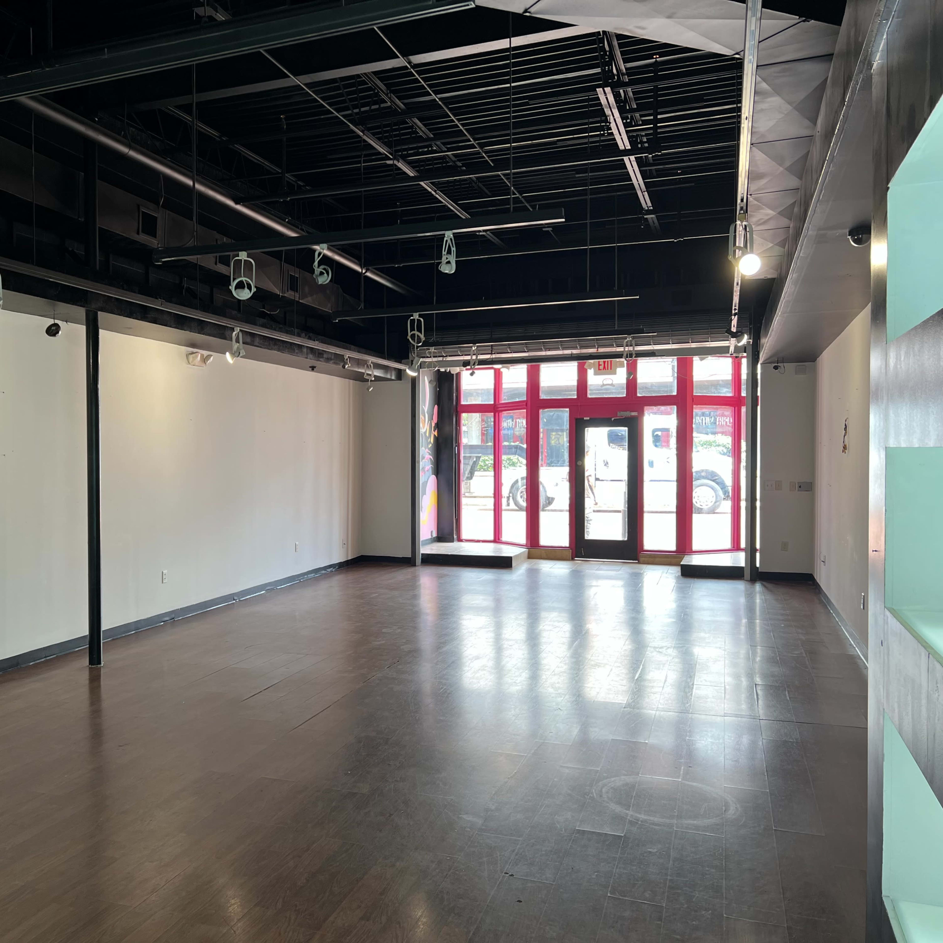 An empty commercial space with a polished wooden floor and large front windows providing natural light.