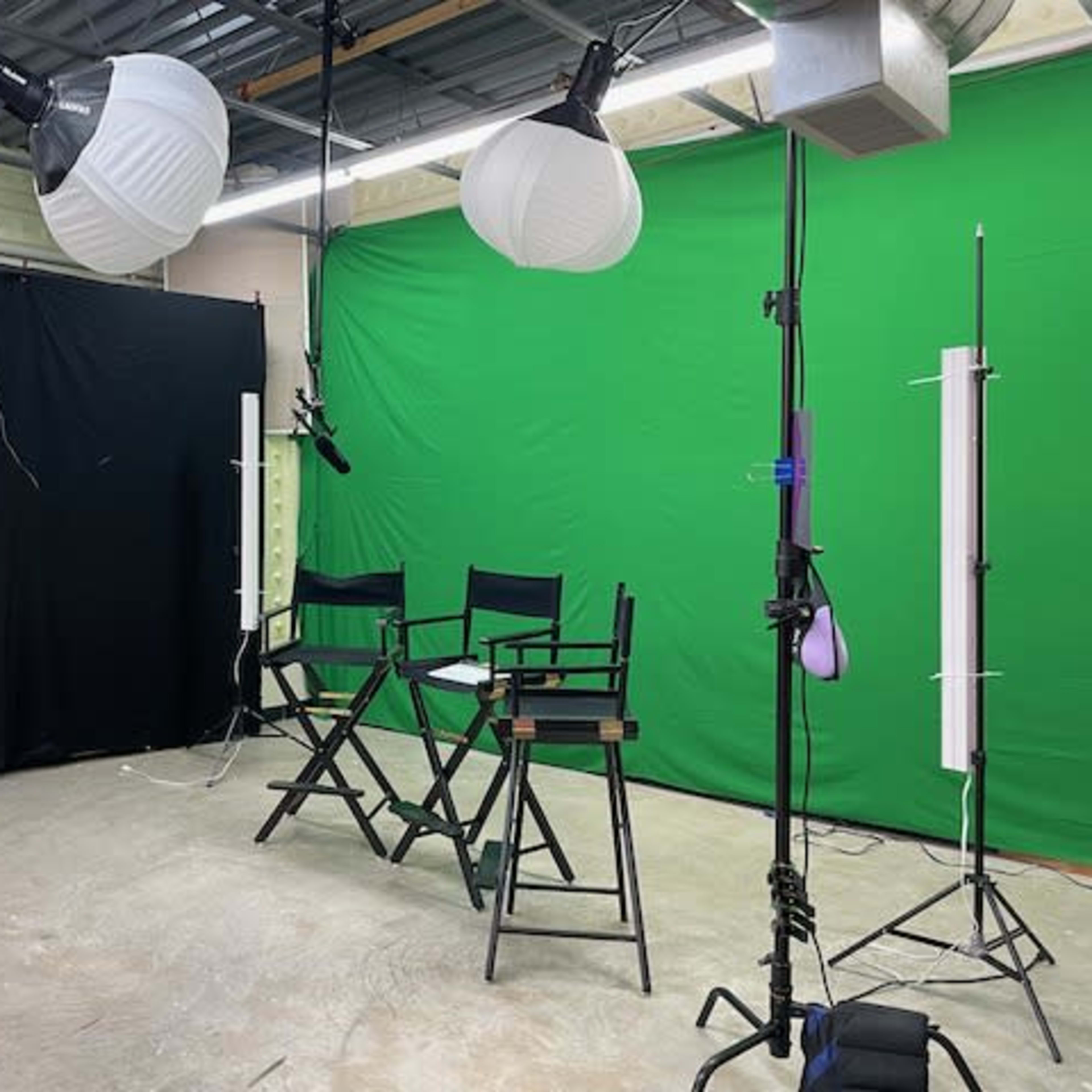 A video production studio with two black director's chairs, green and black backdrops, and lighting equipment.