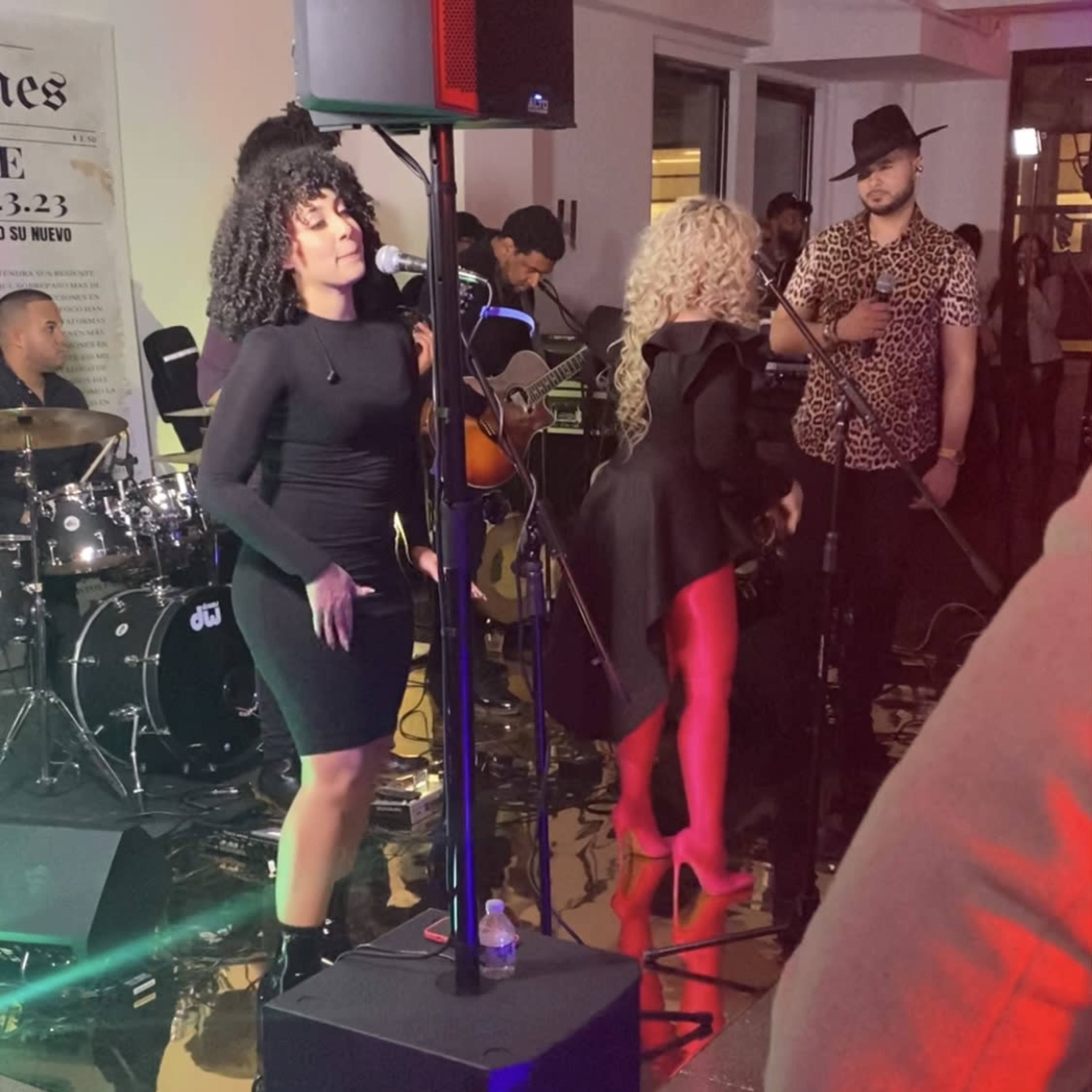 A live music performance is taking place, featuring female vocalists and a band in a venue with a reflective floor.