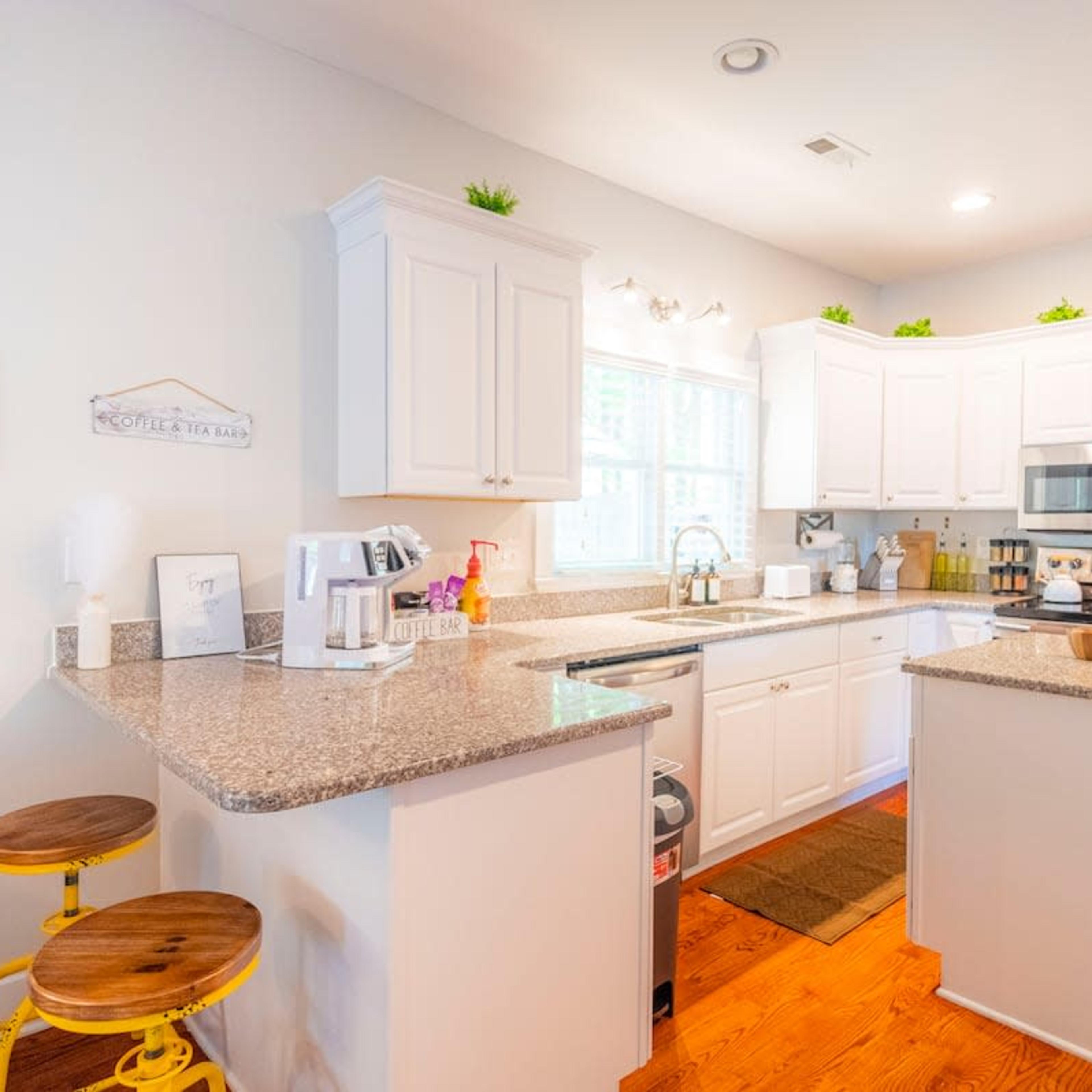 A modern kitchen features white cabinetry, a granite countertop, and stainless steel appliances, with bar stools at the island.
