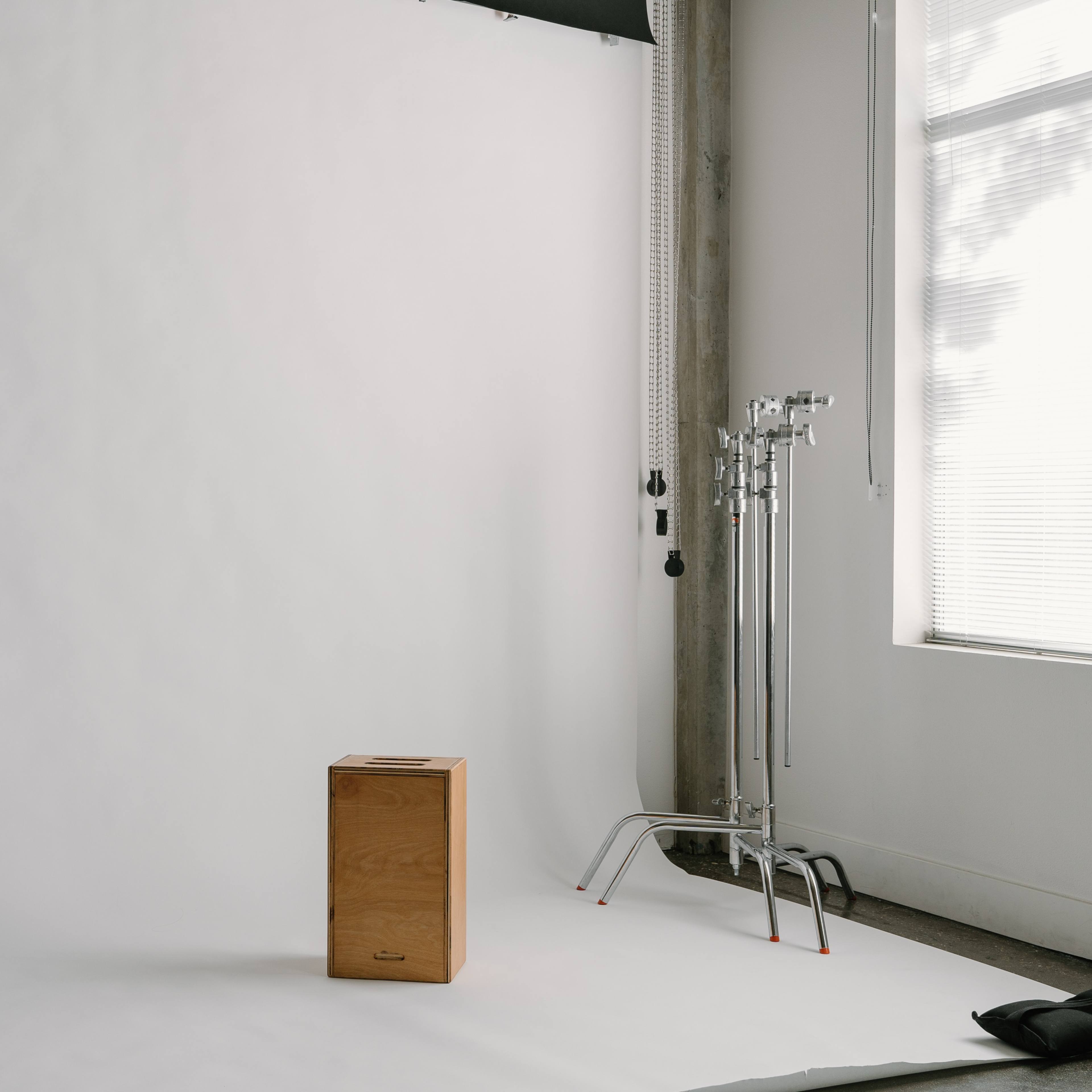 A minimalist photo studio with a wooden box placed in front of a white backdrop and studio equipment nearby.