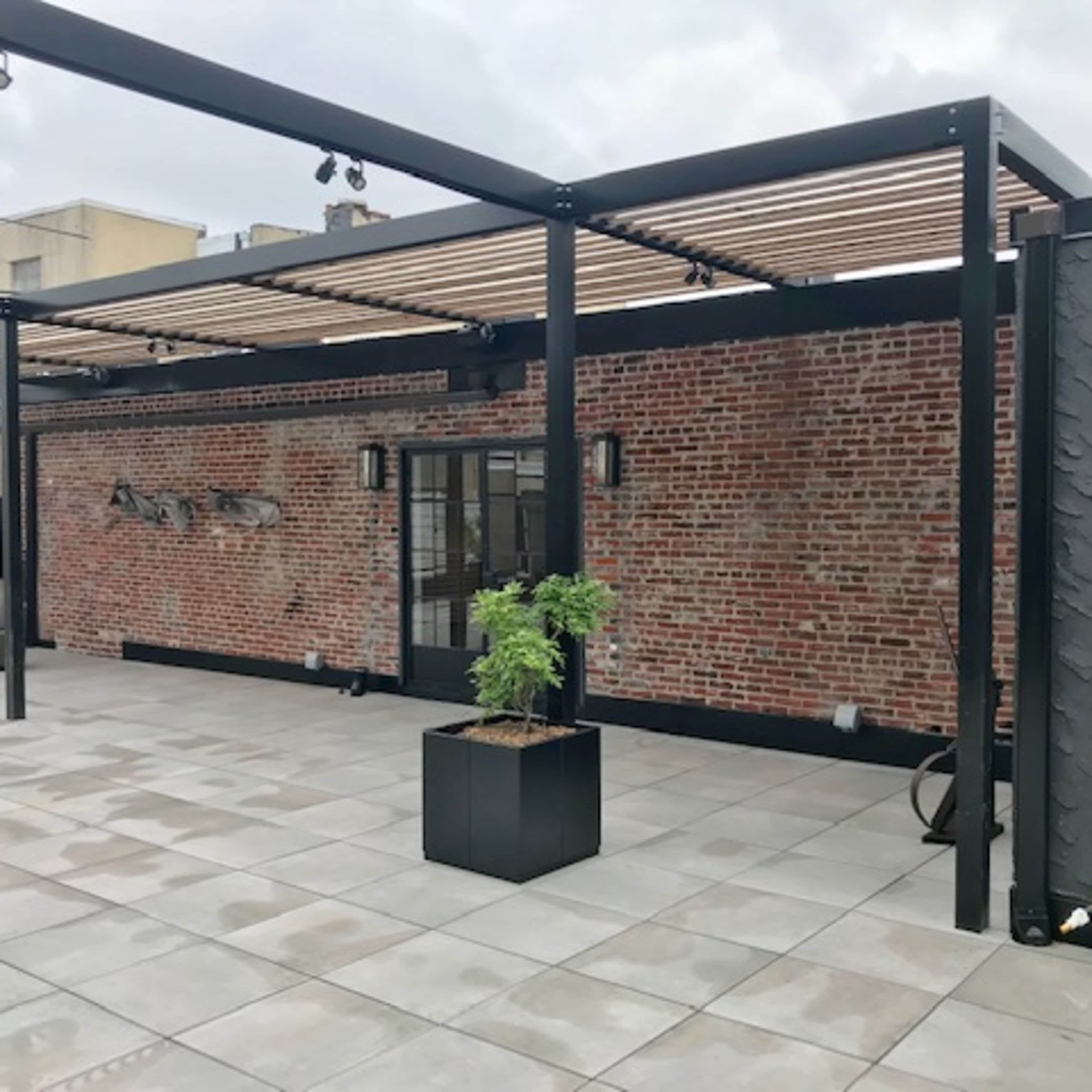 A rooftop area with a landscaped design featuring a stone-tiled floor, a brick wall, and an overhead pergola.