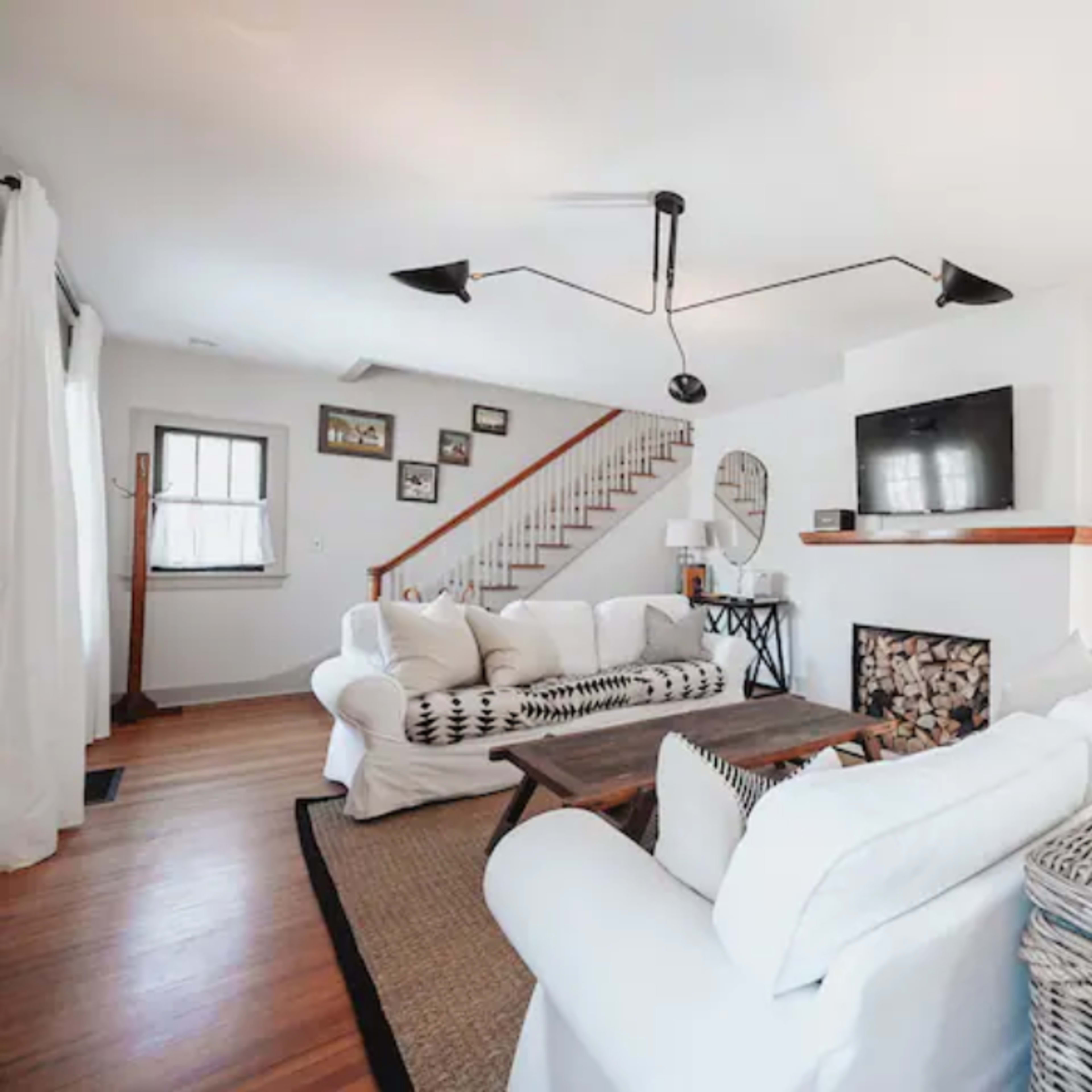 The living room features a white sectional sofa, a wooden coffee table, a fireplace, and a staircase in the background.