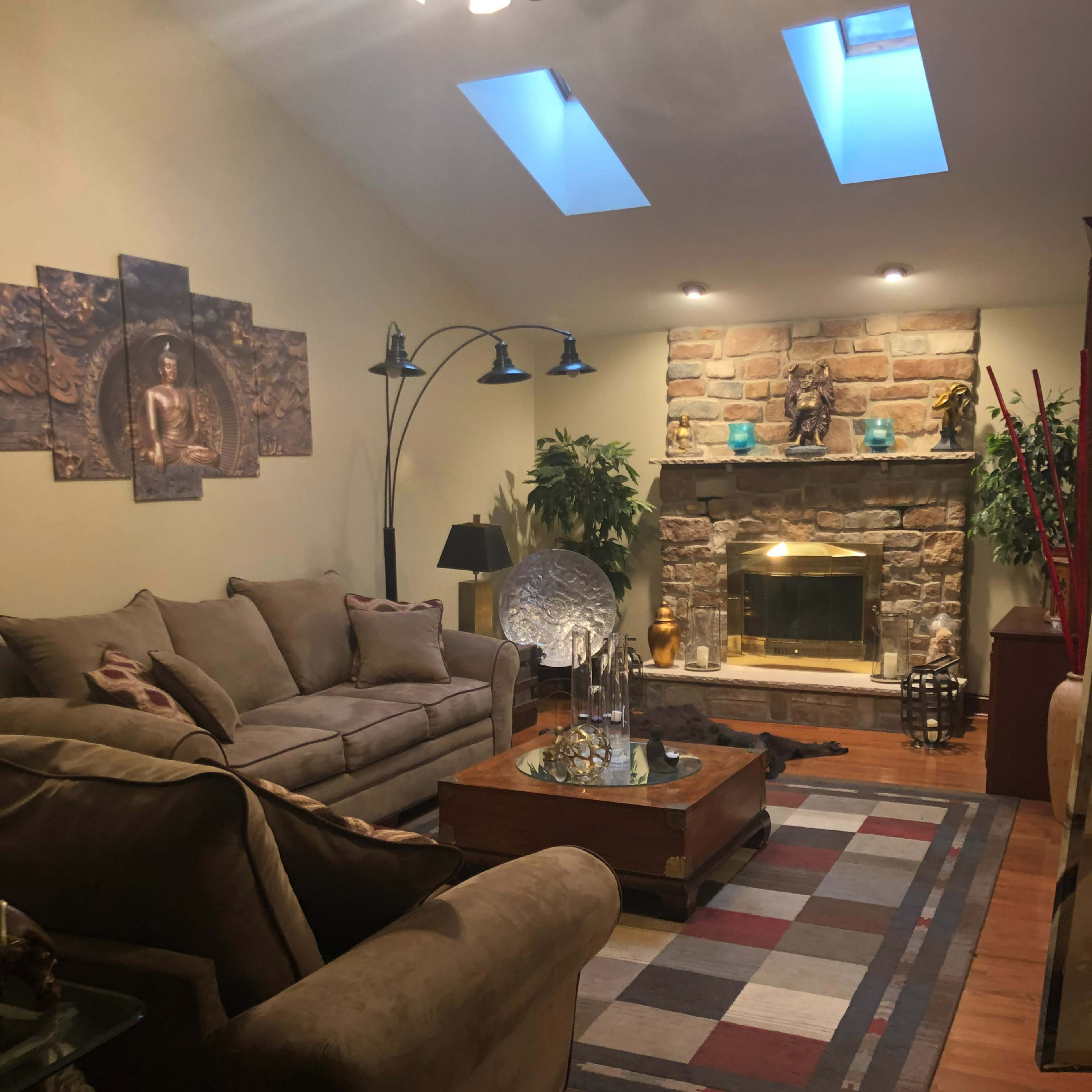 The room features a cozy seating arrangement with a large sofa, a coffee table, and a stone fireplace, illuminated by natural light through skylights.