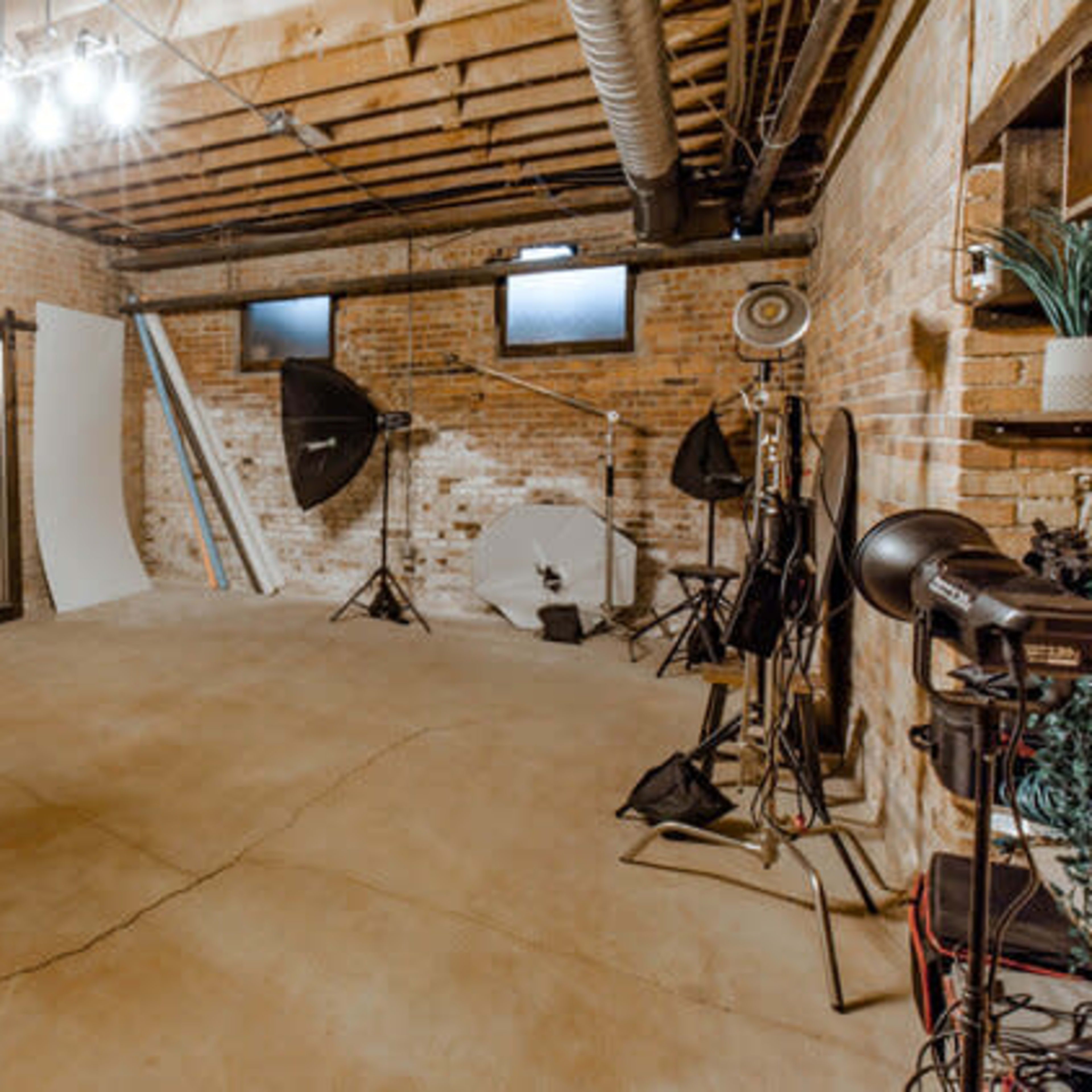 A spacious, well-lit photography studio featuring brick walls, a concrete floor, and various equipment set up for shooting.
