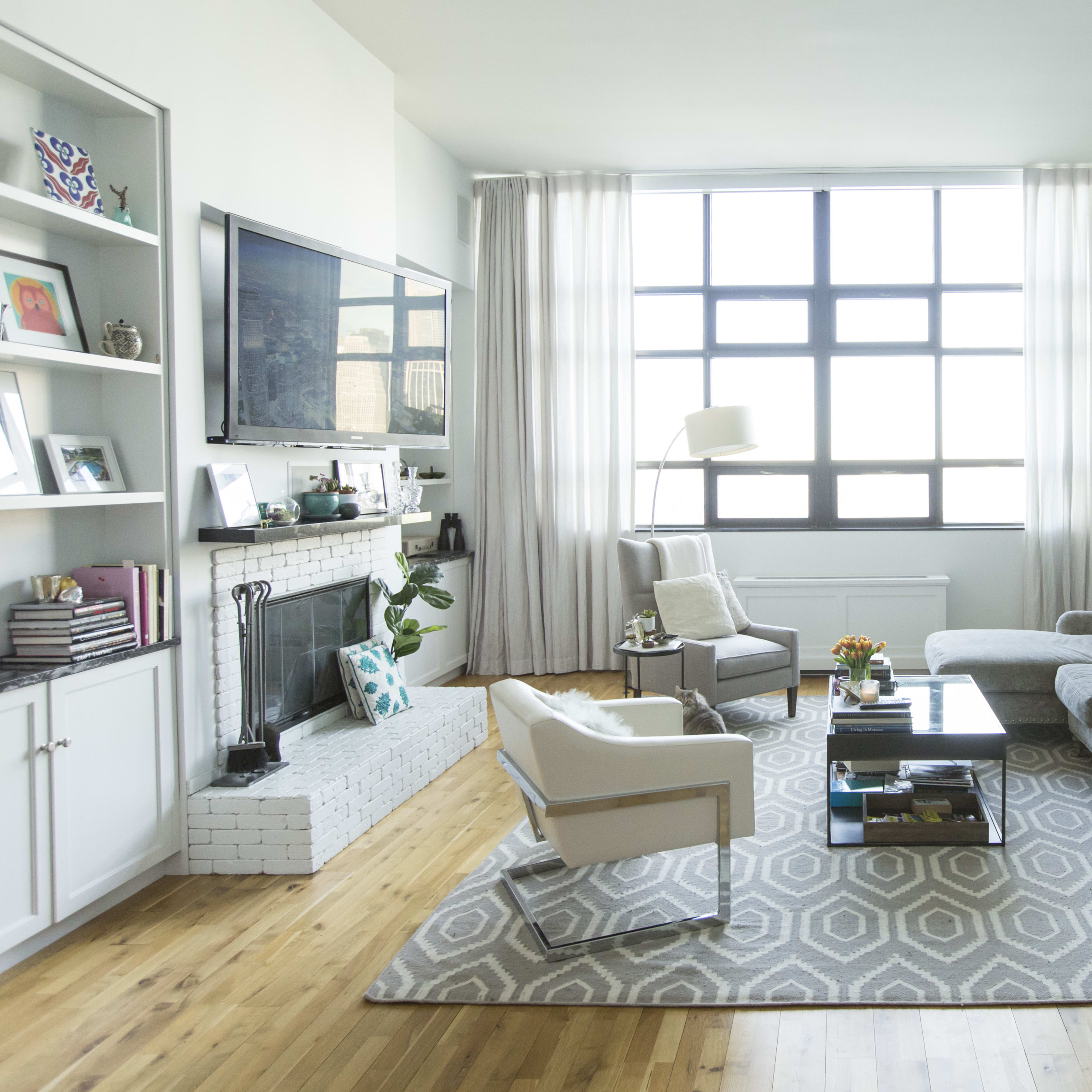 A modern living room with a large window, a gray sectional sofa, a coffee table, and a green abstract painting on the wall.