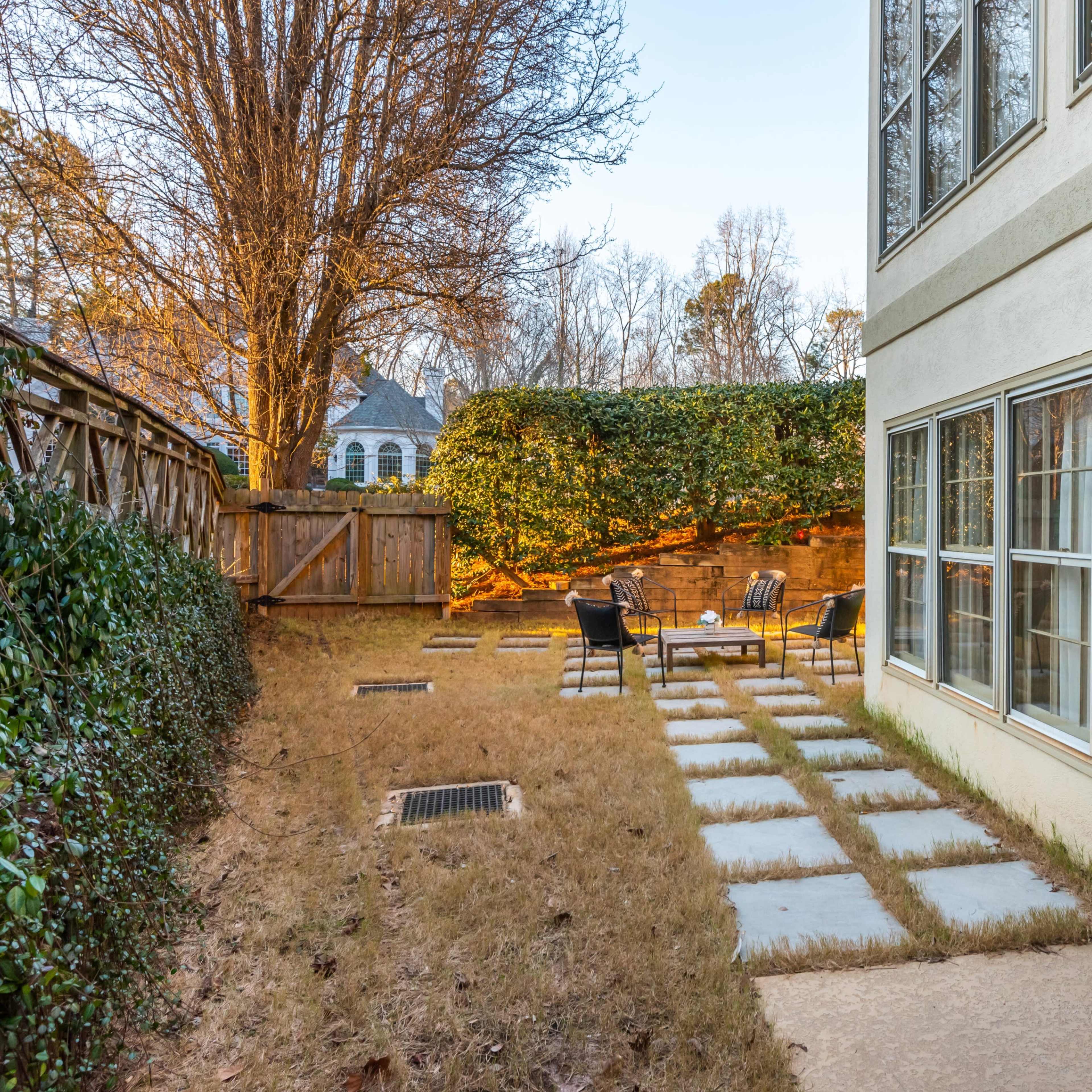 A backyard area with a stone pathway leading to a seating arrangement surrounded by grass and shrubbery.