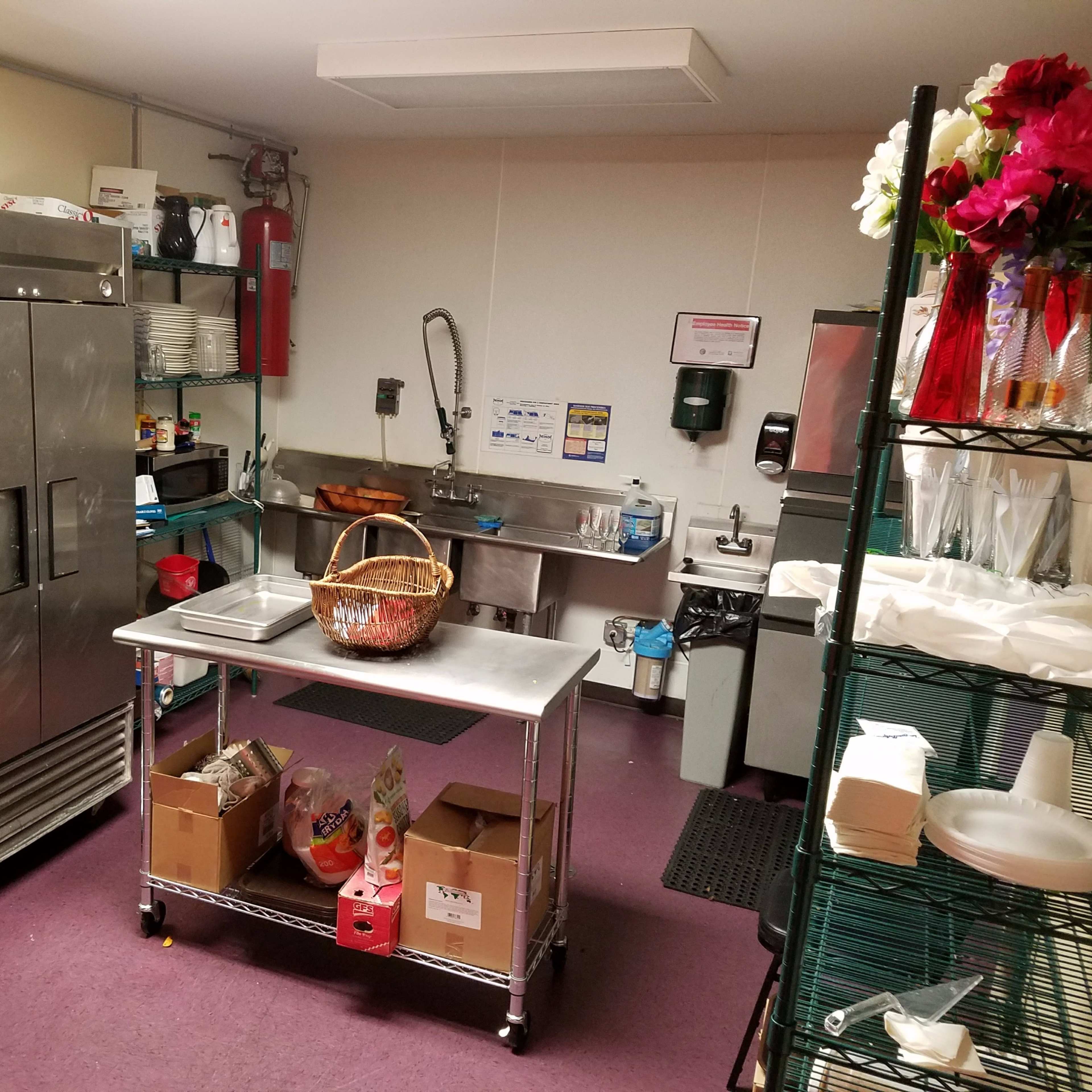 A kitchen space with stainless steel appliances, a worktable, and a sink area, along with various supplies and a basket on the counter.