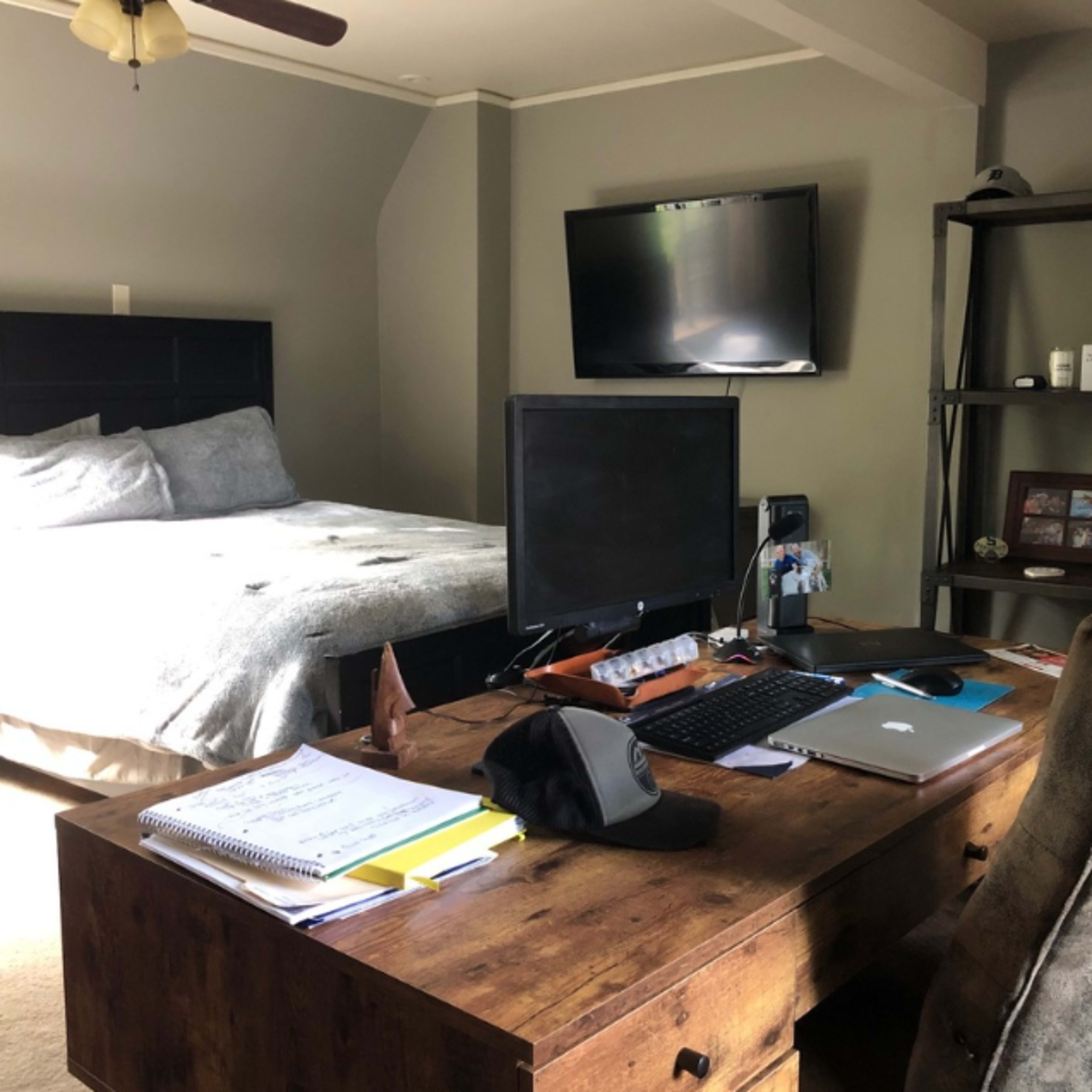 A bedroom with a bed, a desk with a computer, and a wall-mounted television.