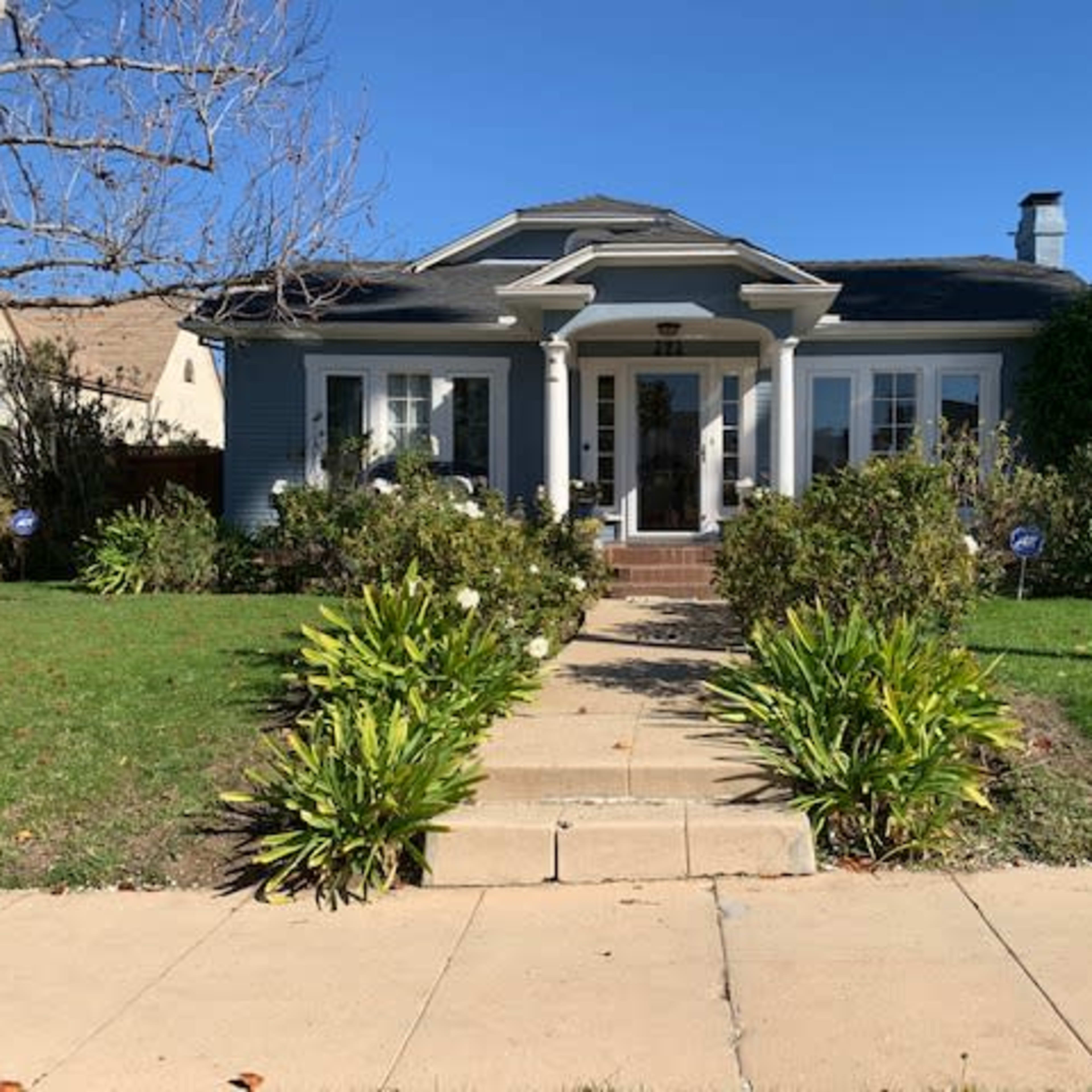 A single-story house with a front porch, surrounded by shrubs and a manicured lawn, is visible on a clear day.