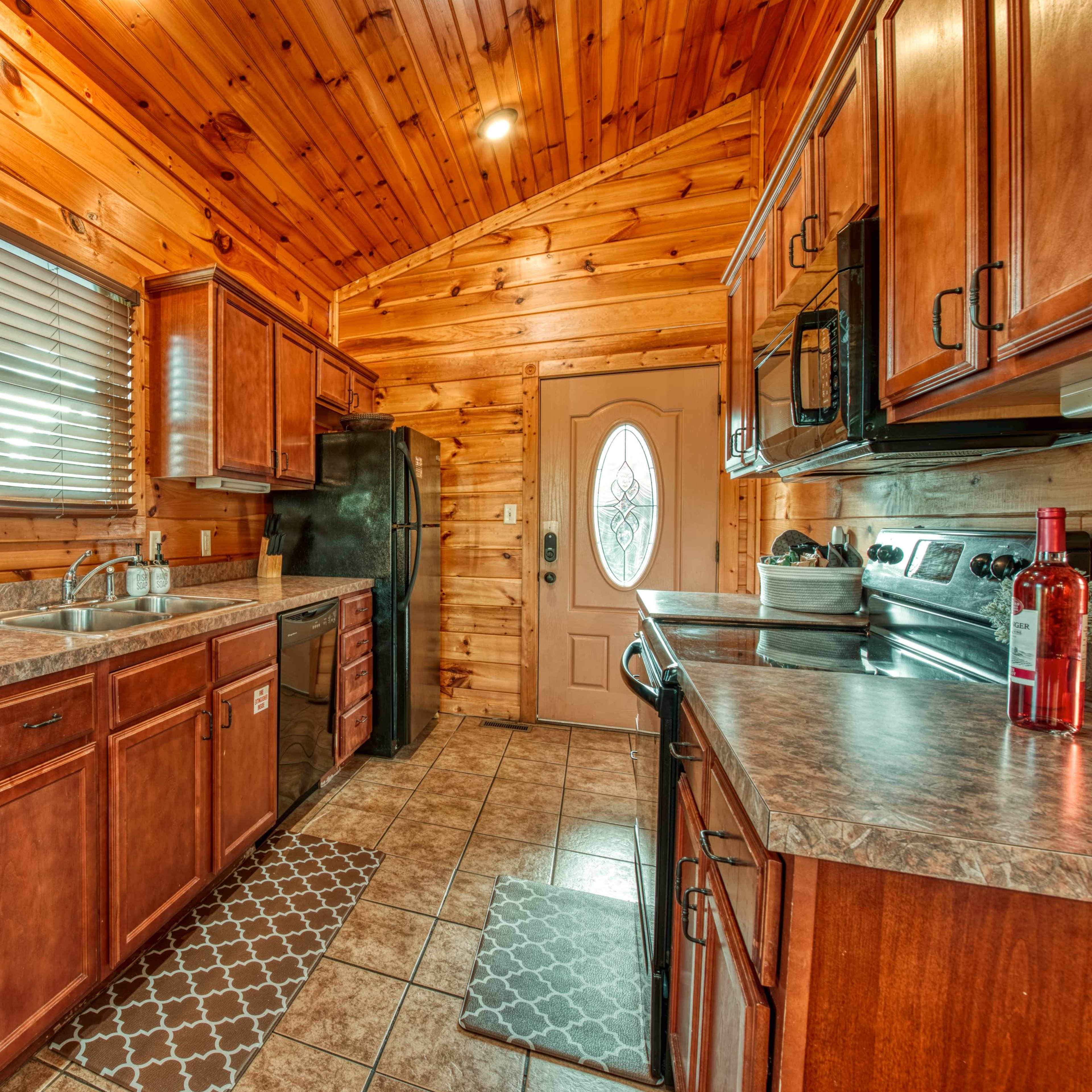 The kitchen features wooden cabinets, tile flooring, and stainless steel appliances, with a door leading outside.
