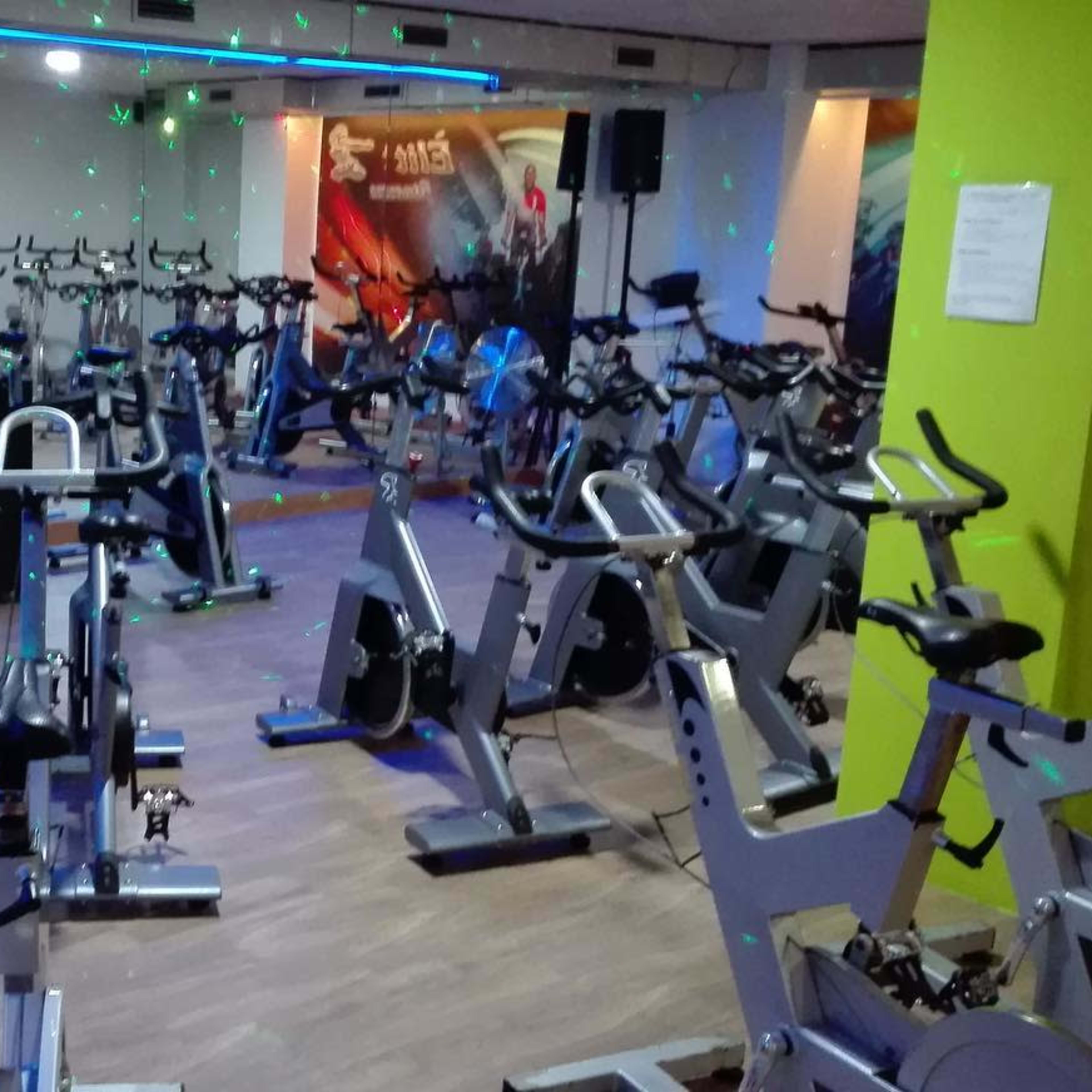 A fitness studio is filled with stationary bicycles and illuminated by colorful lights.