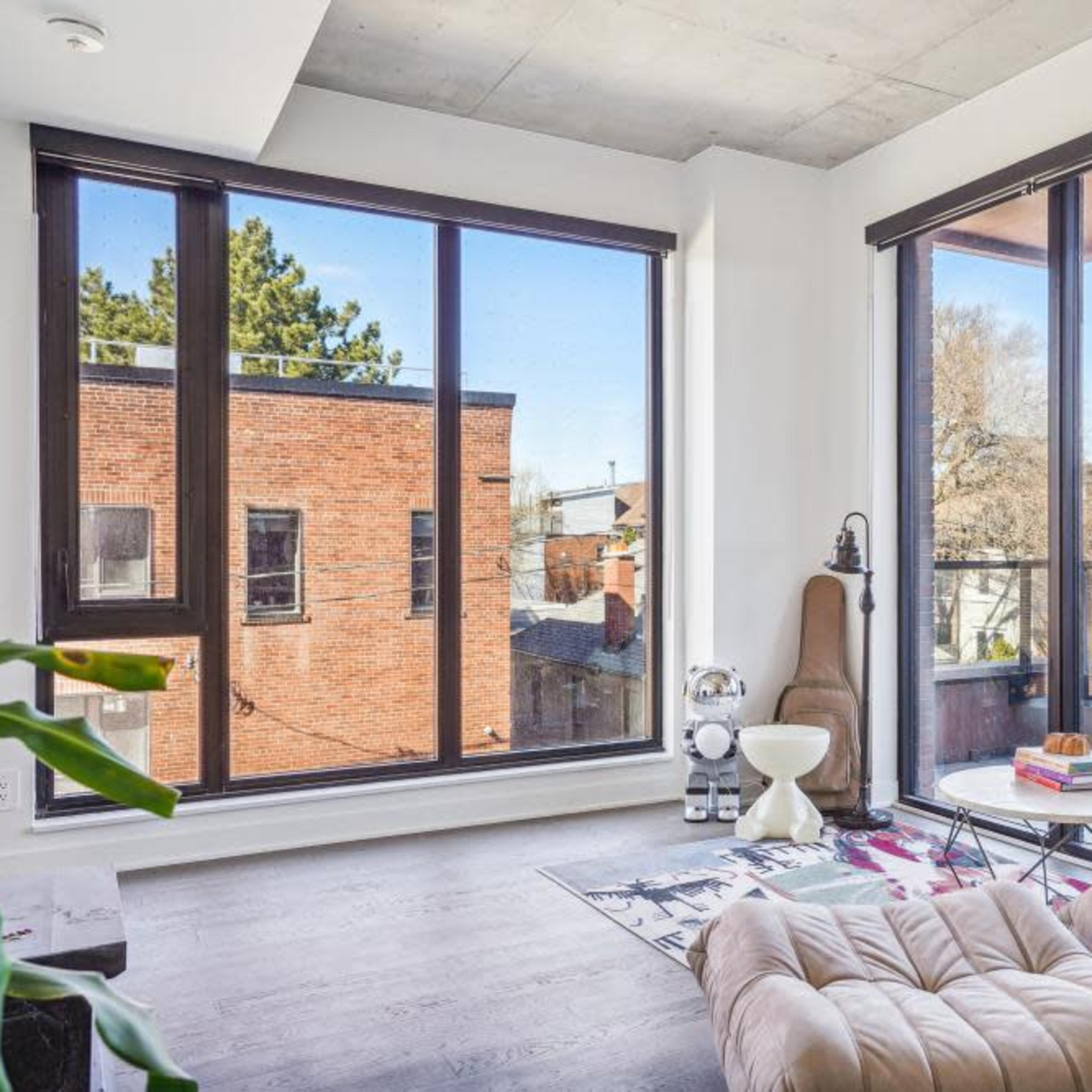 A modern living room with large windows allowing natural light to fill the space, featuring a cozy chair and a small table.