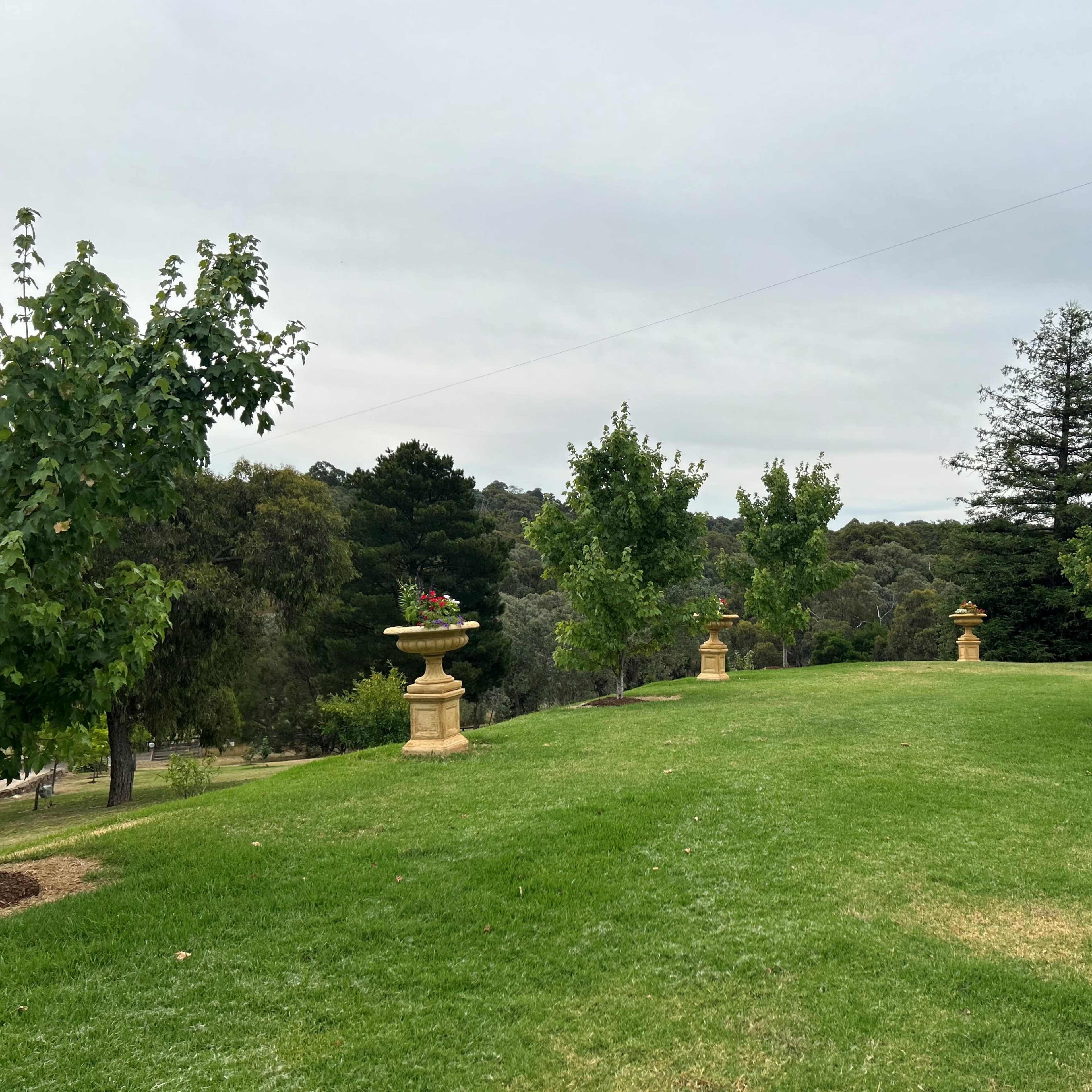 A manicured lawn with ornamental stone planters and scattered trees under a cloudy sky.