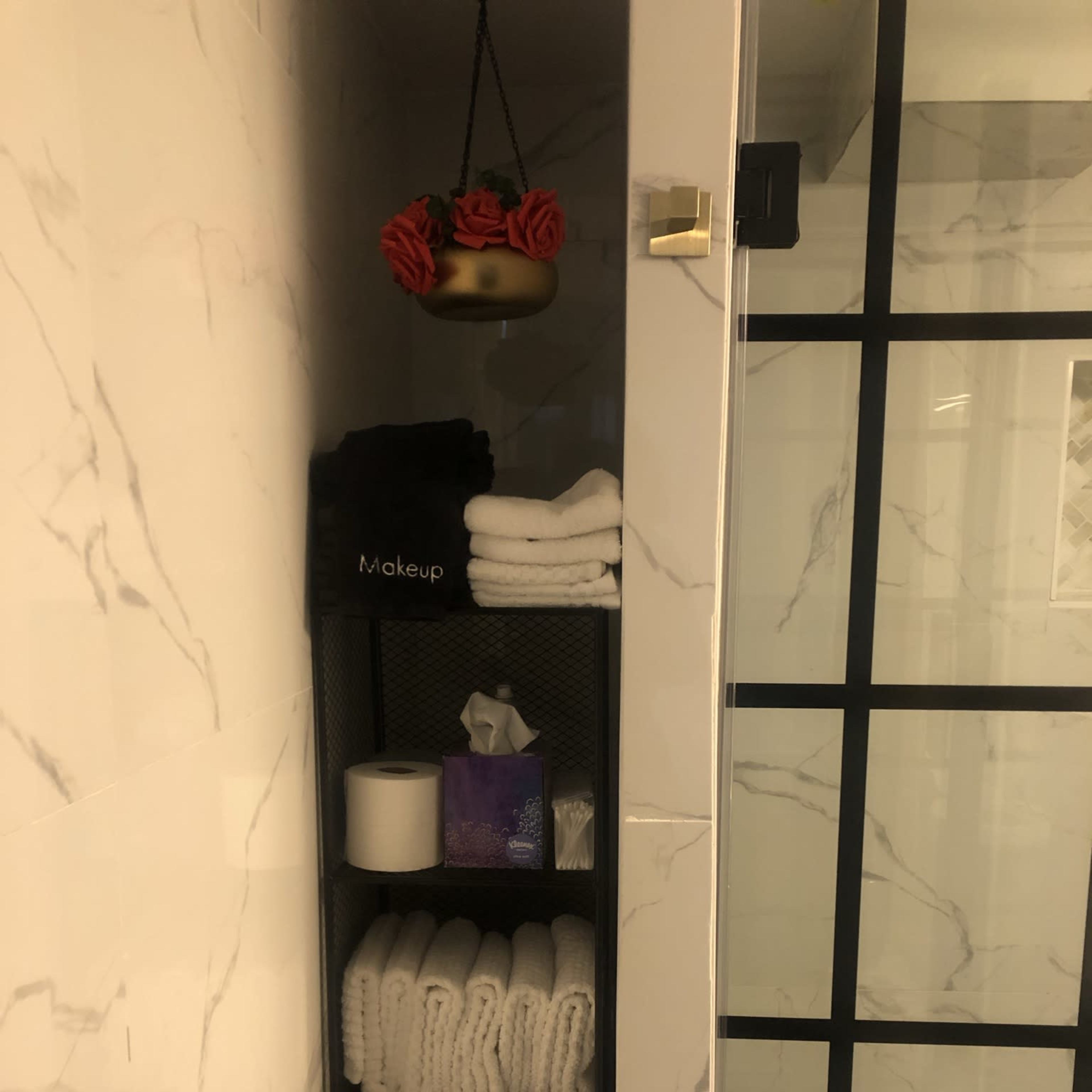 A storage shelf in a bathroom with neatly arranged white towels, a roll of toilet paper, and a box of tissues.