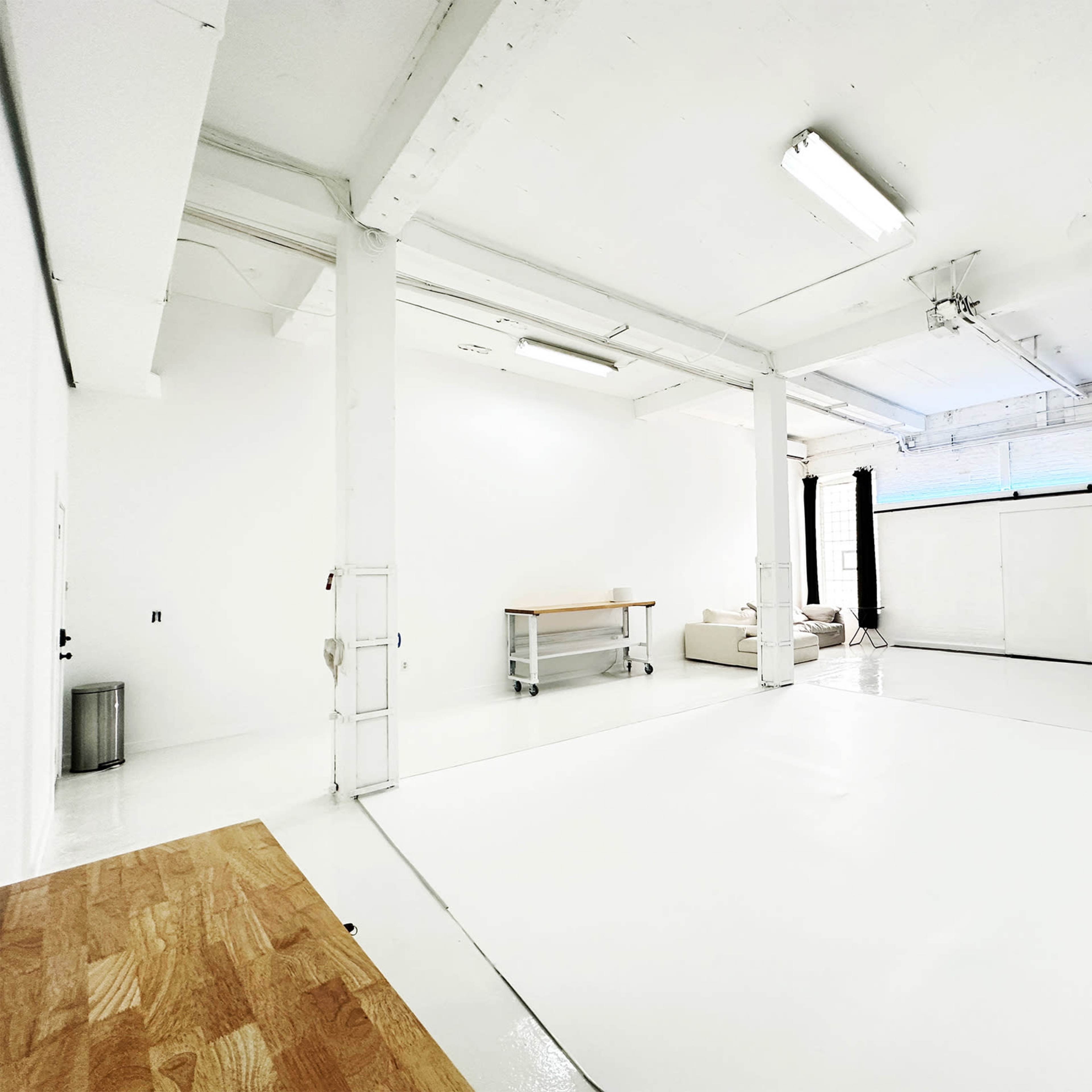 A spacious, white studio with a seamless backdrop, bright lighting, and minimal furnishings including a table and a couch.
