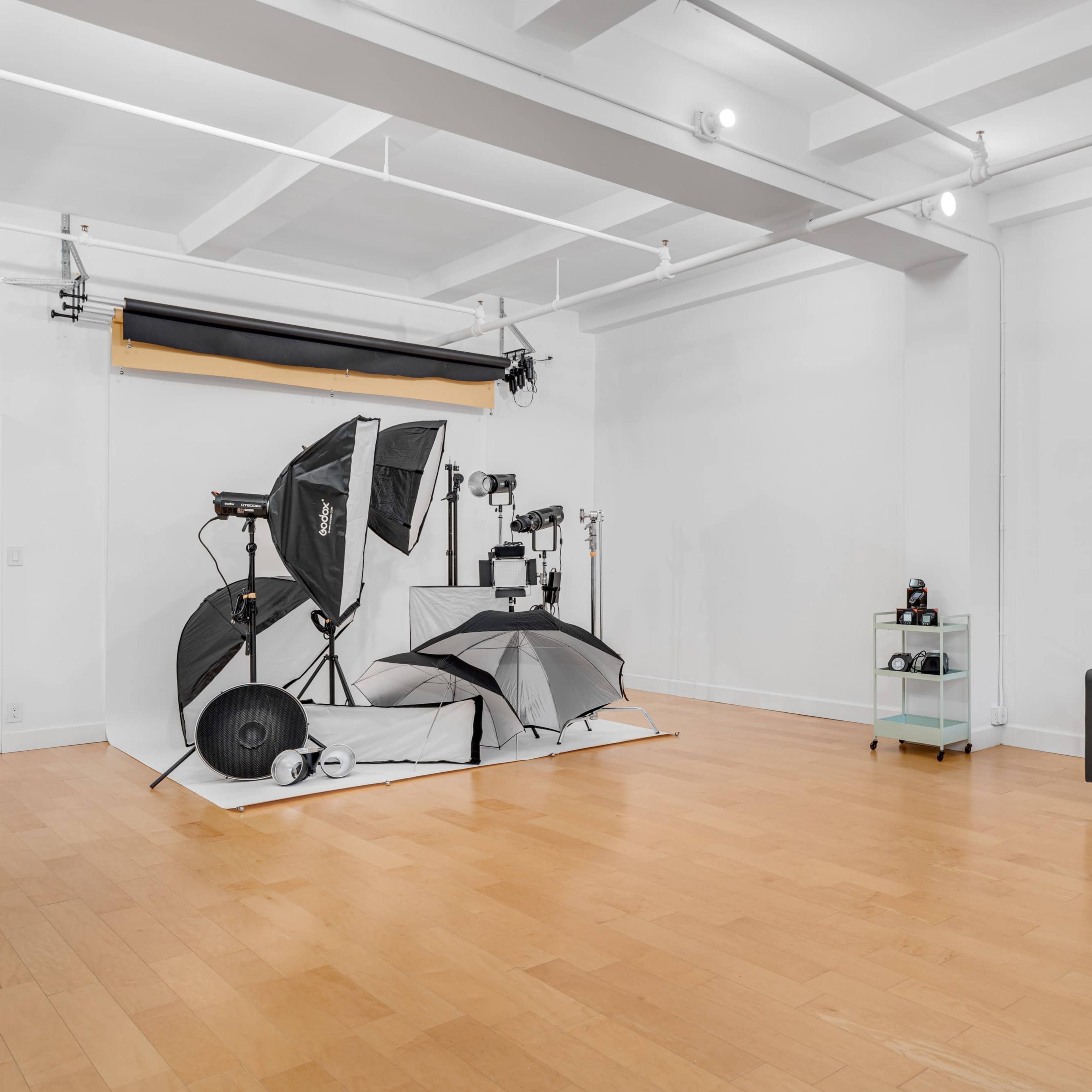 A spacious studio with a gray couch and photography lighting equipment arranged on a backdrop.