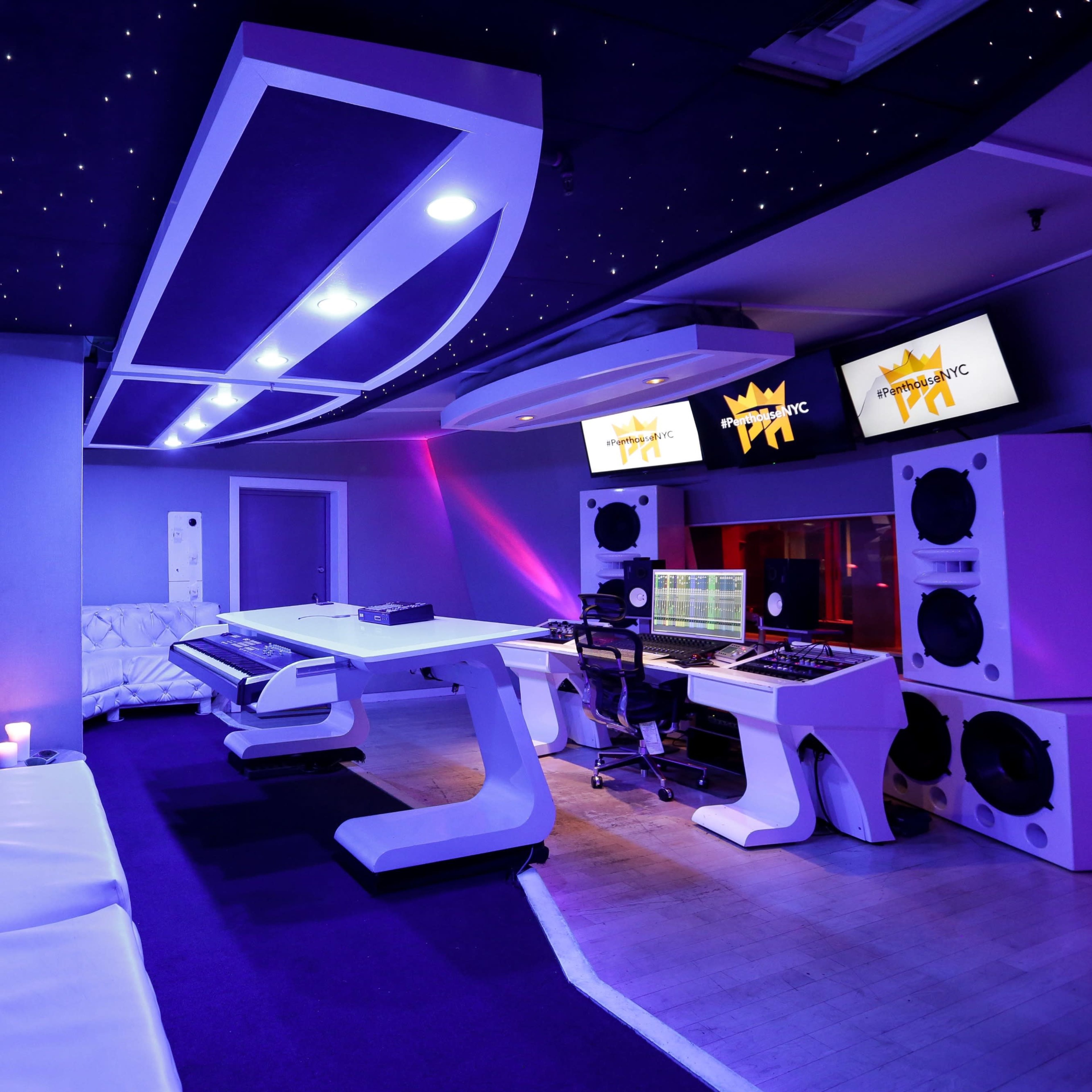 A modern recording studio with sleek white furniture, a large sound mixing console, and two computer screens displaying sound software, all under a starry ceiling.