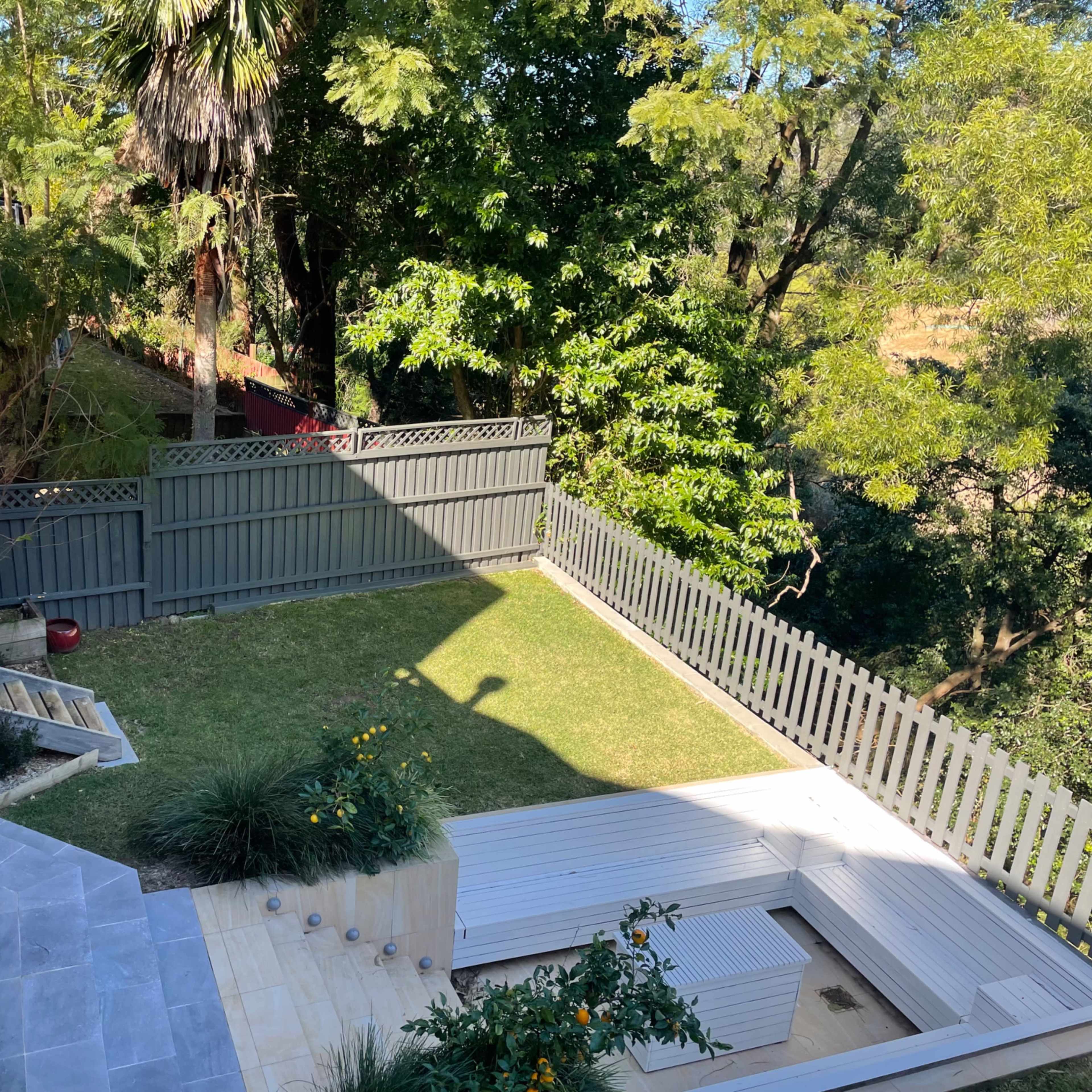 A landscaped backyard with a grassy area, a wooden deck, and surrounding trees, viewed from an elevated angle.