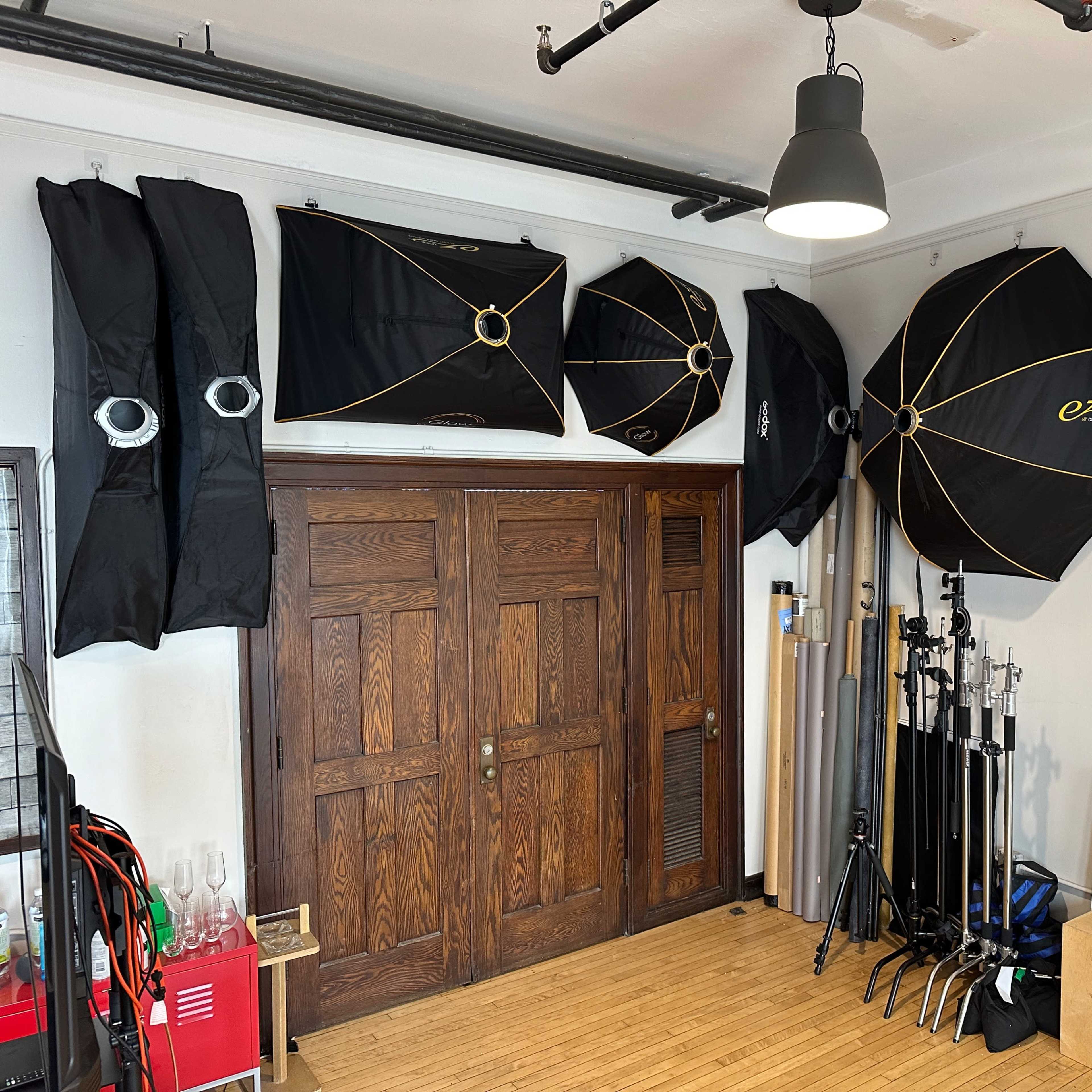 A room with several photography light umbrellas mounted on the walls, alongside various photography gear and props stored on the floor.