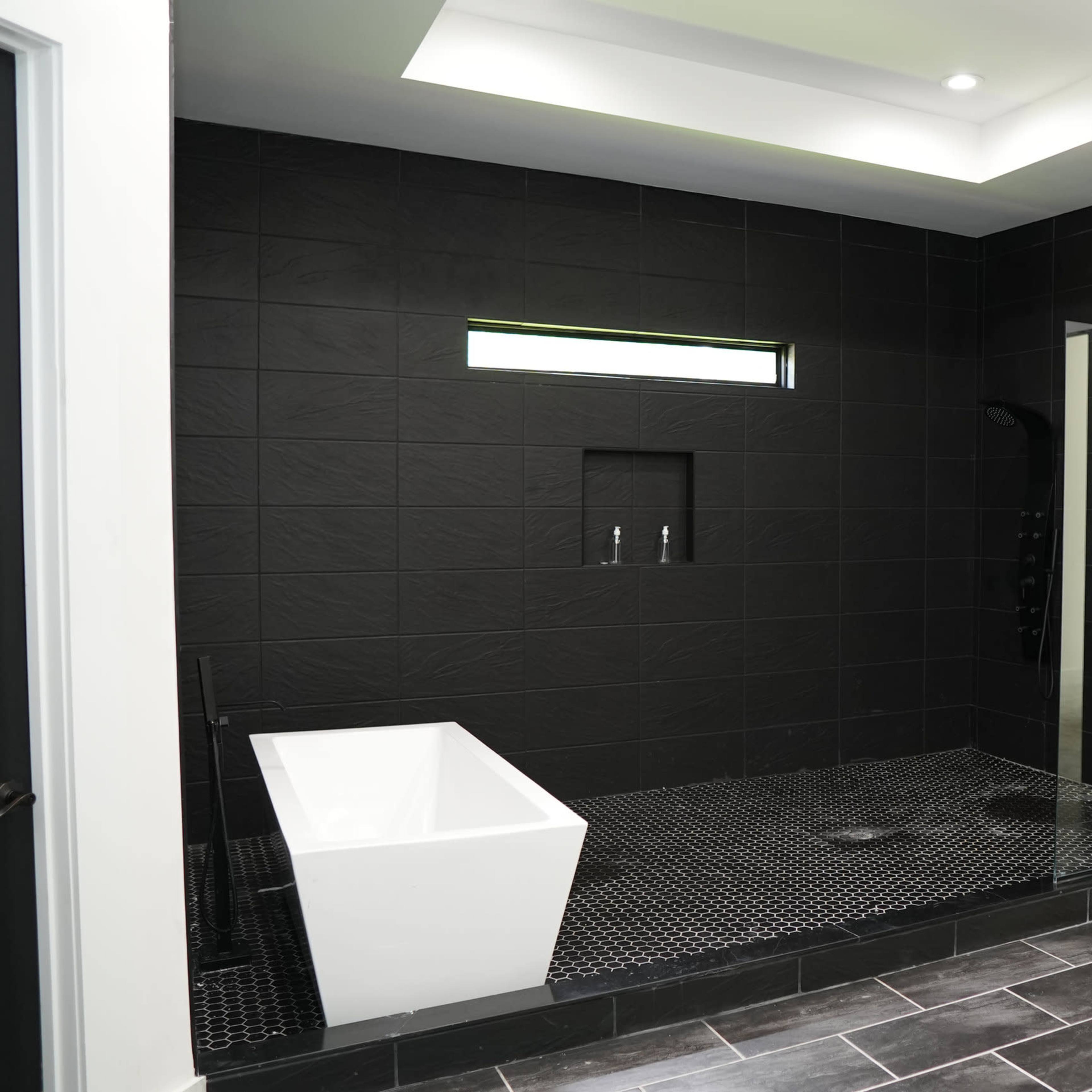A bathroom with a freestanding white bathtub, a large walk-in shower, and black tiled walls and flooring.