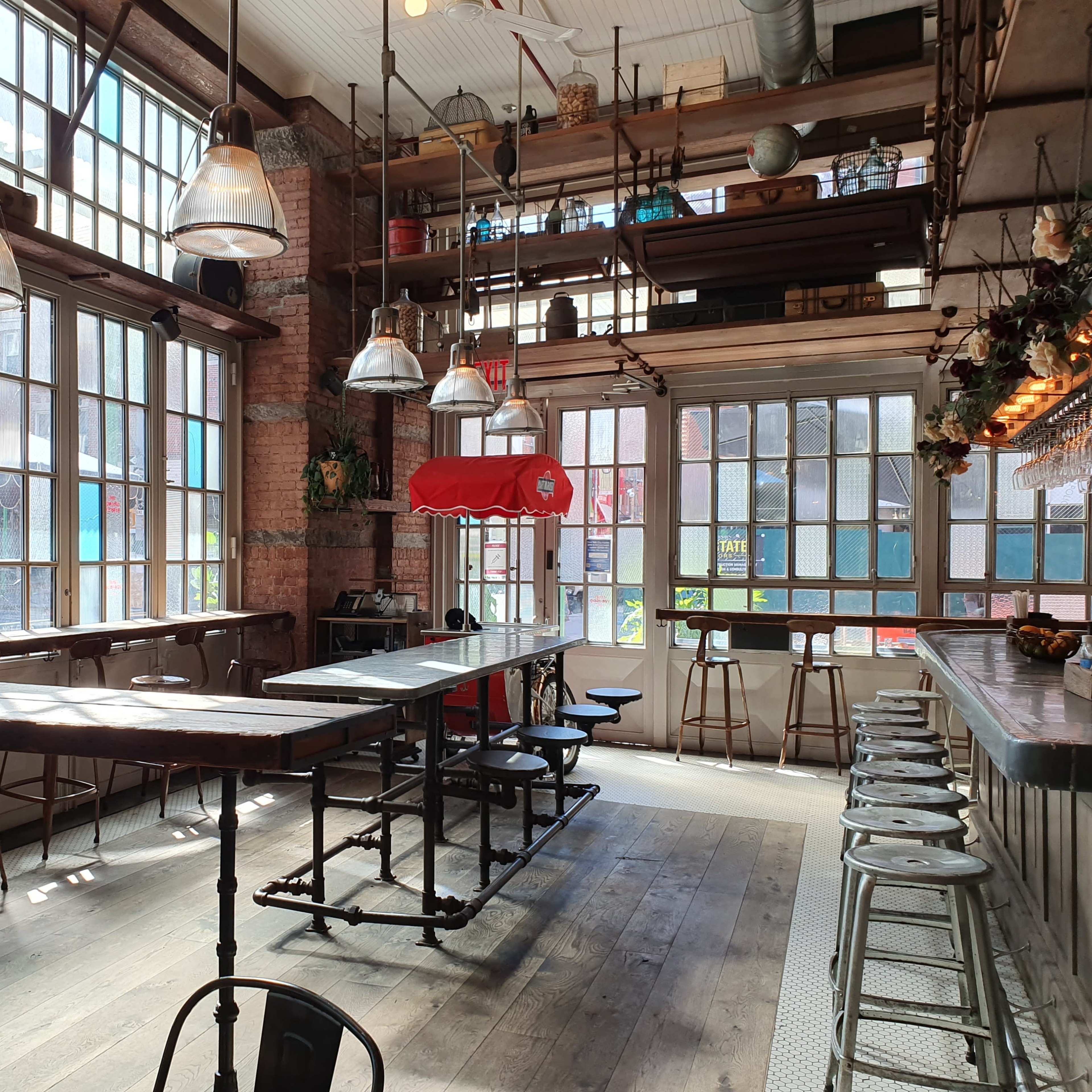 A spacious, industrial-style café with large windows, wooden flooring, and a long bar with stools.
