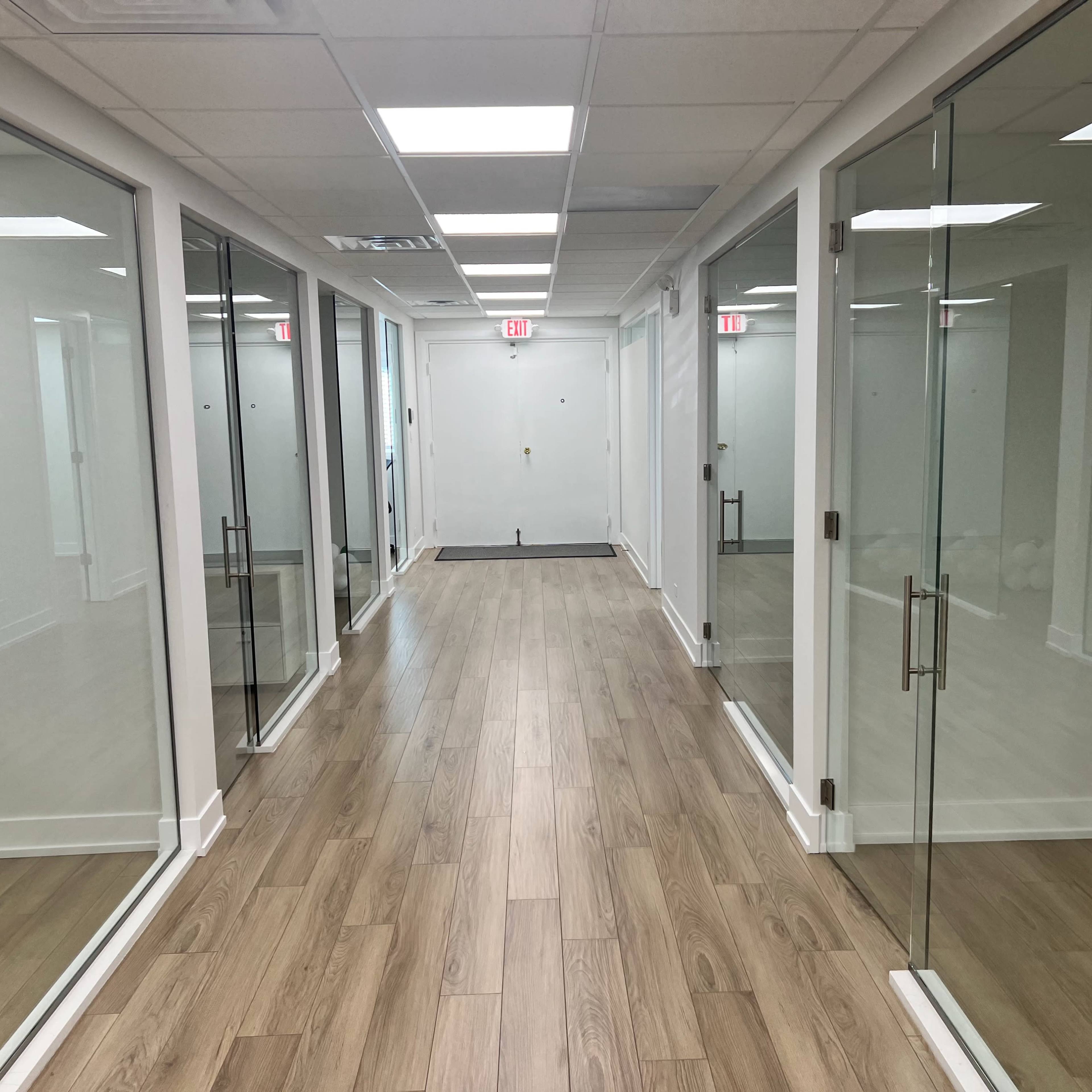 A hallway features glass-walled offices on both sides and a wooden floor.
