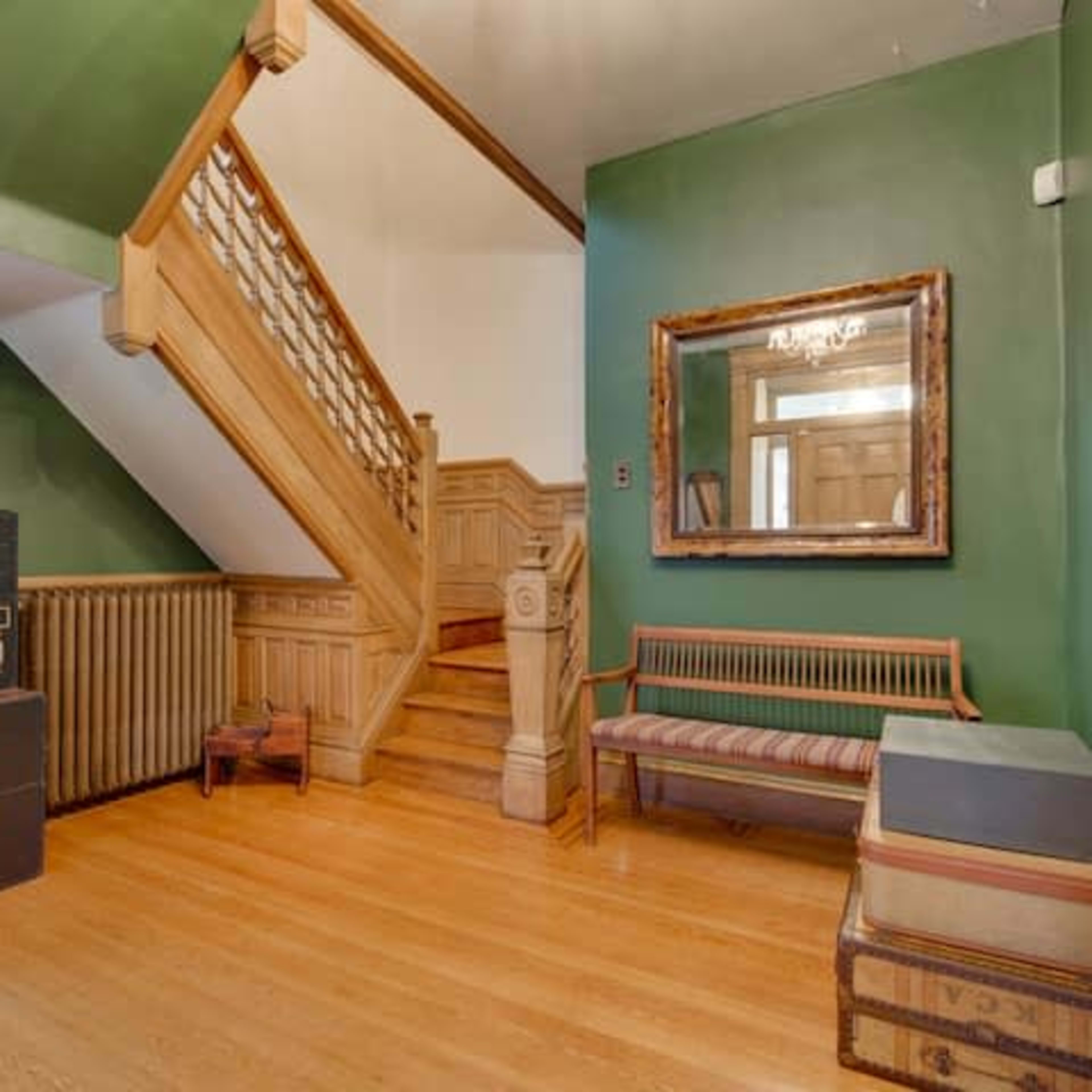 The entryway features a staircase, a wooden bench, and a storage chest against green walls.
