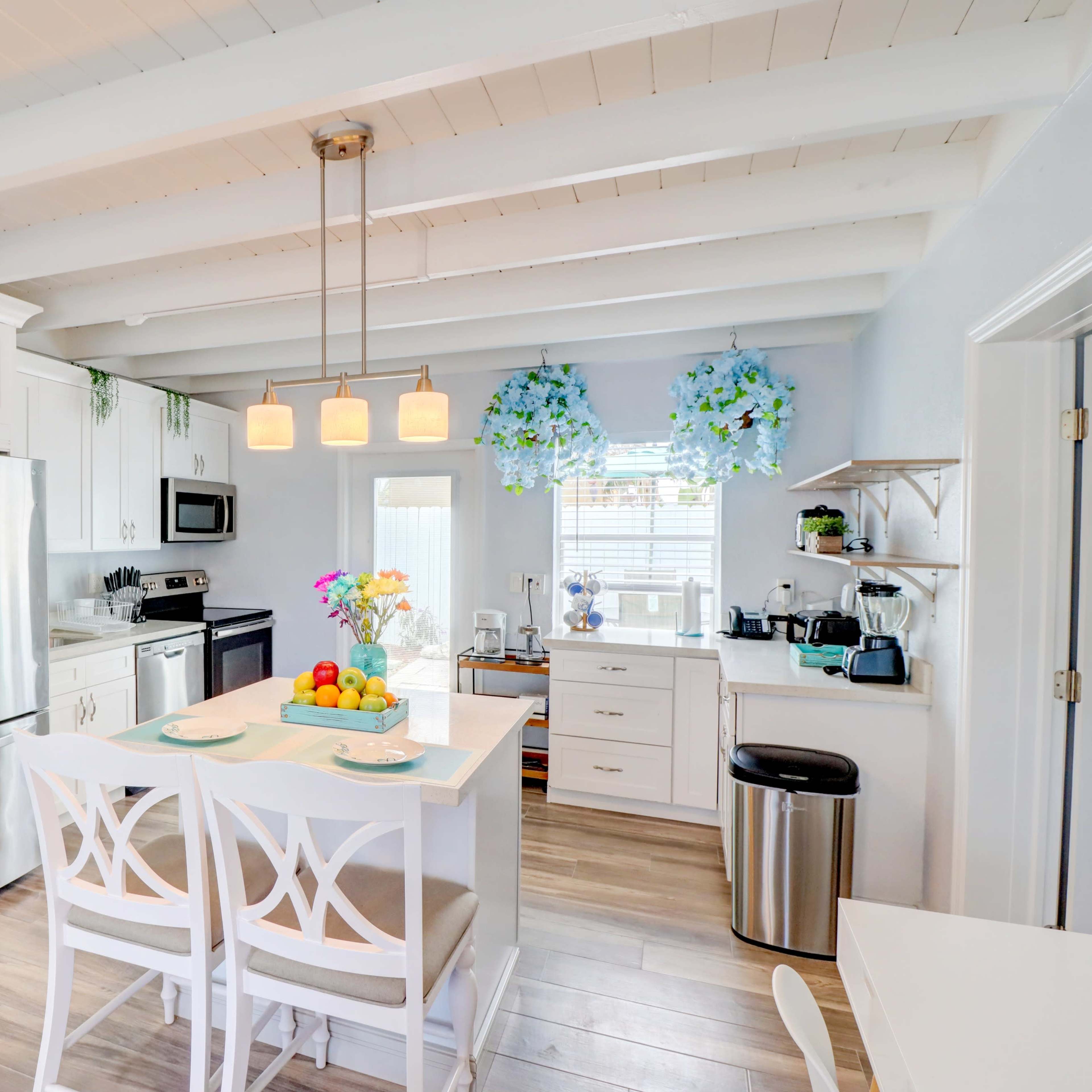 The kitchen features white cabinetry, stainless steel appliances, and a central island with seating, illuminated by pendant lights.