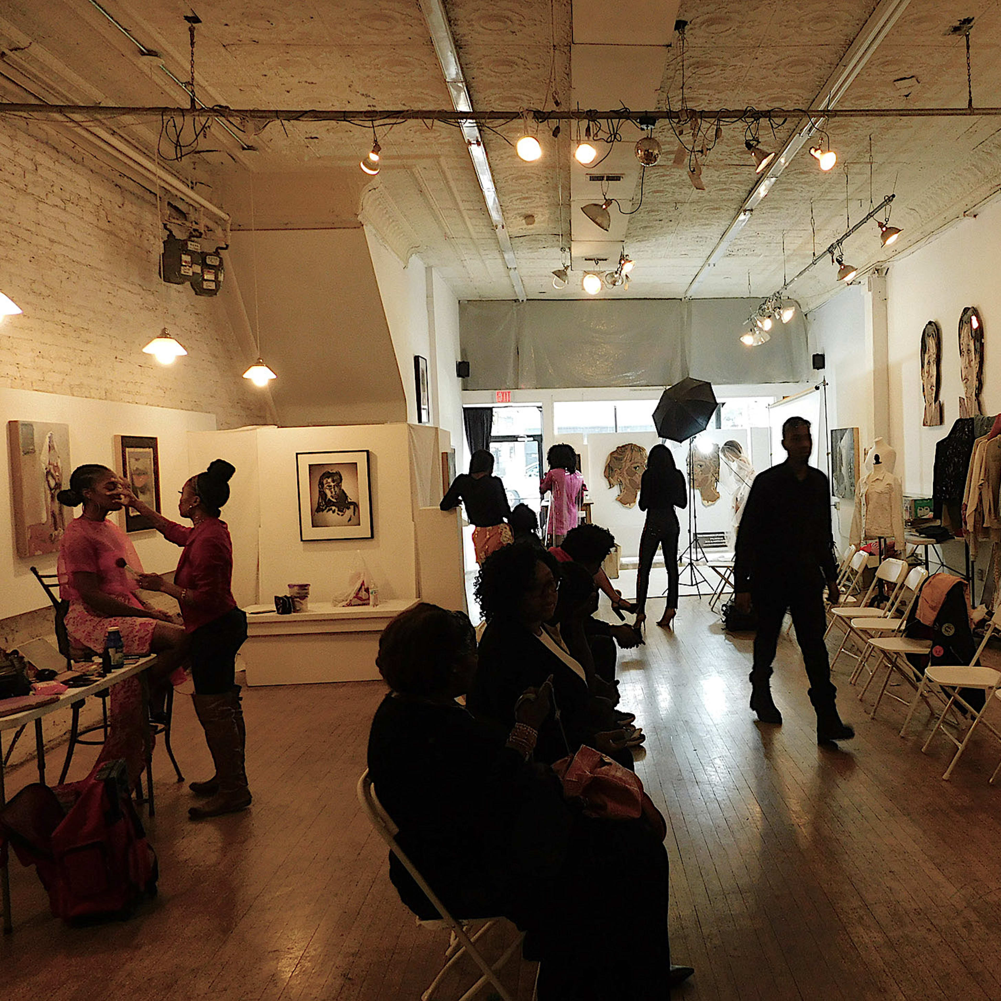 A modern art gallery with several people, chairs, and artworks displayed on the walls.