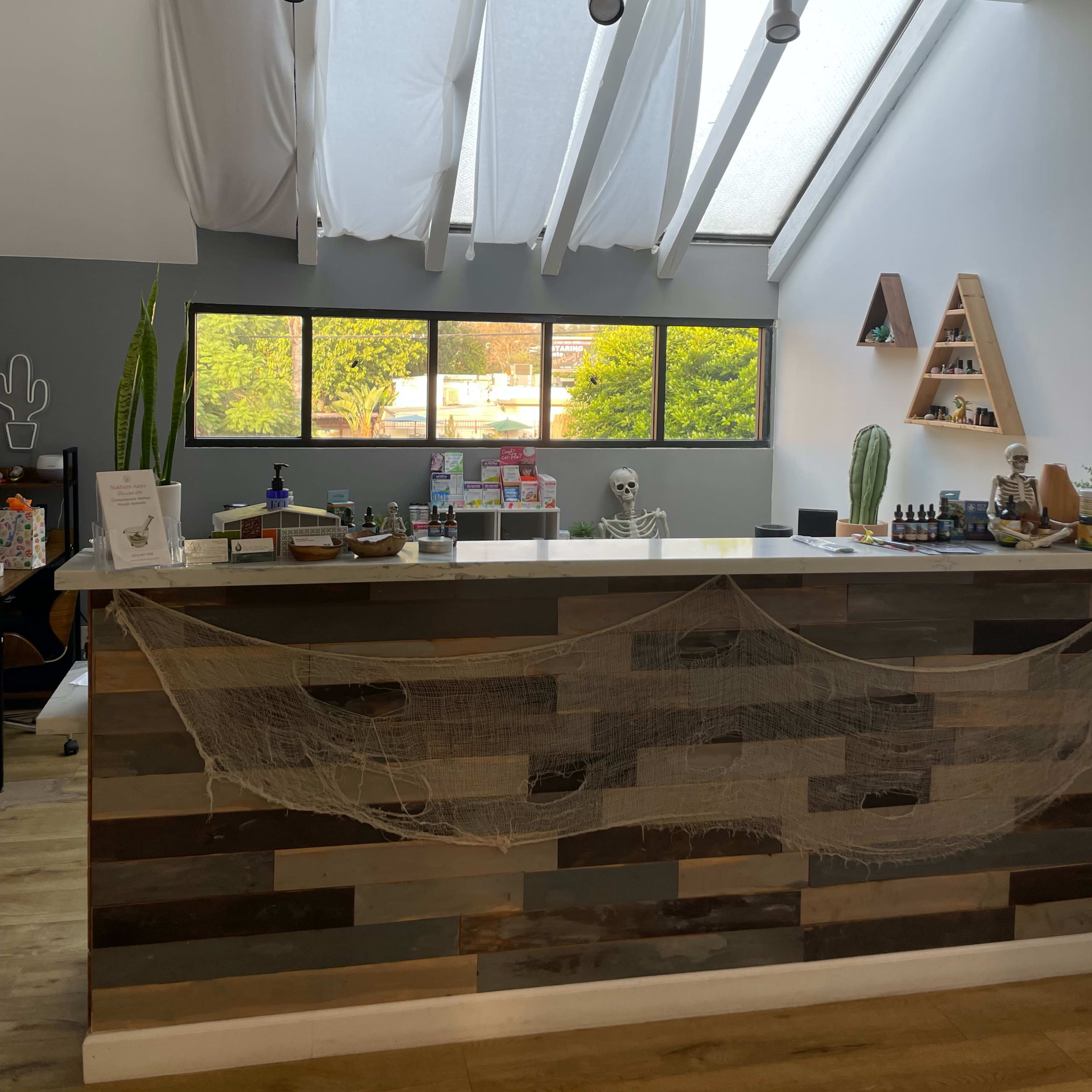 A reception area features a gray wall, large windows, and a wooden counter with decorations, including a skeleton and plants.