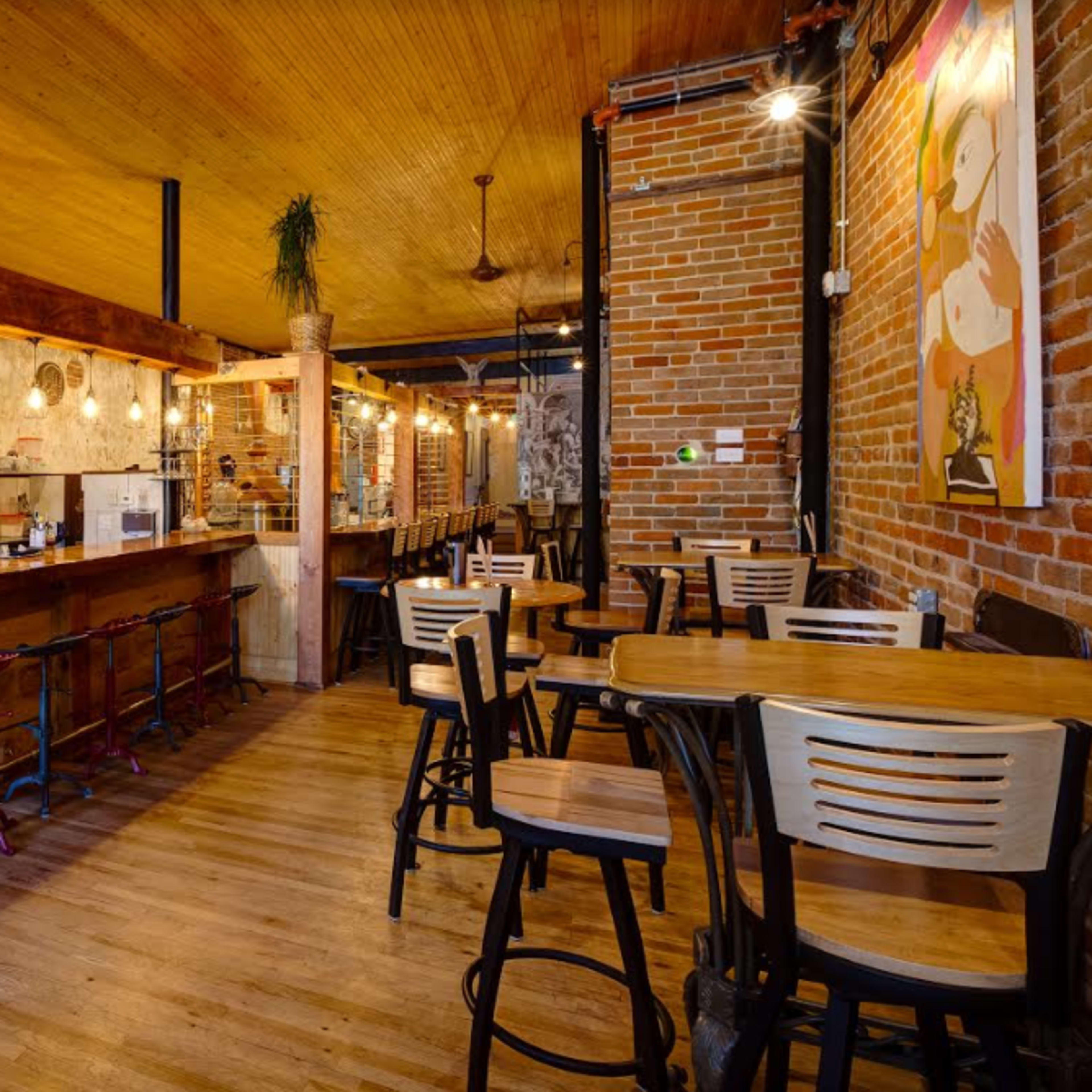 A rustic cafe interior with wooden tables, a bar area, and exposed brick walls.