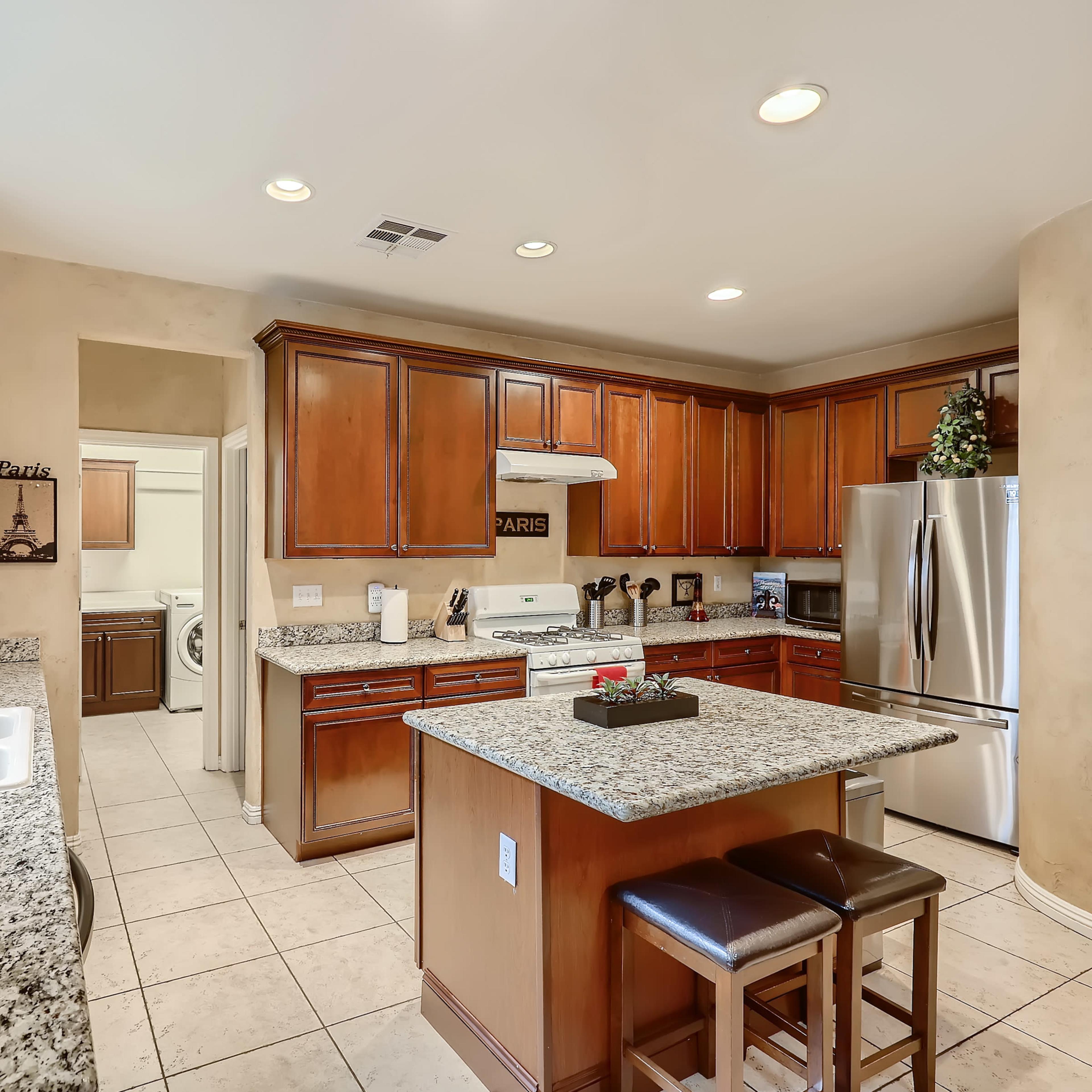 A kitchen with wood cabinets, granite countertops, and a small island with two stools.