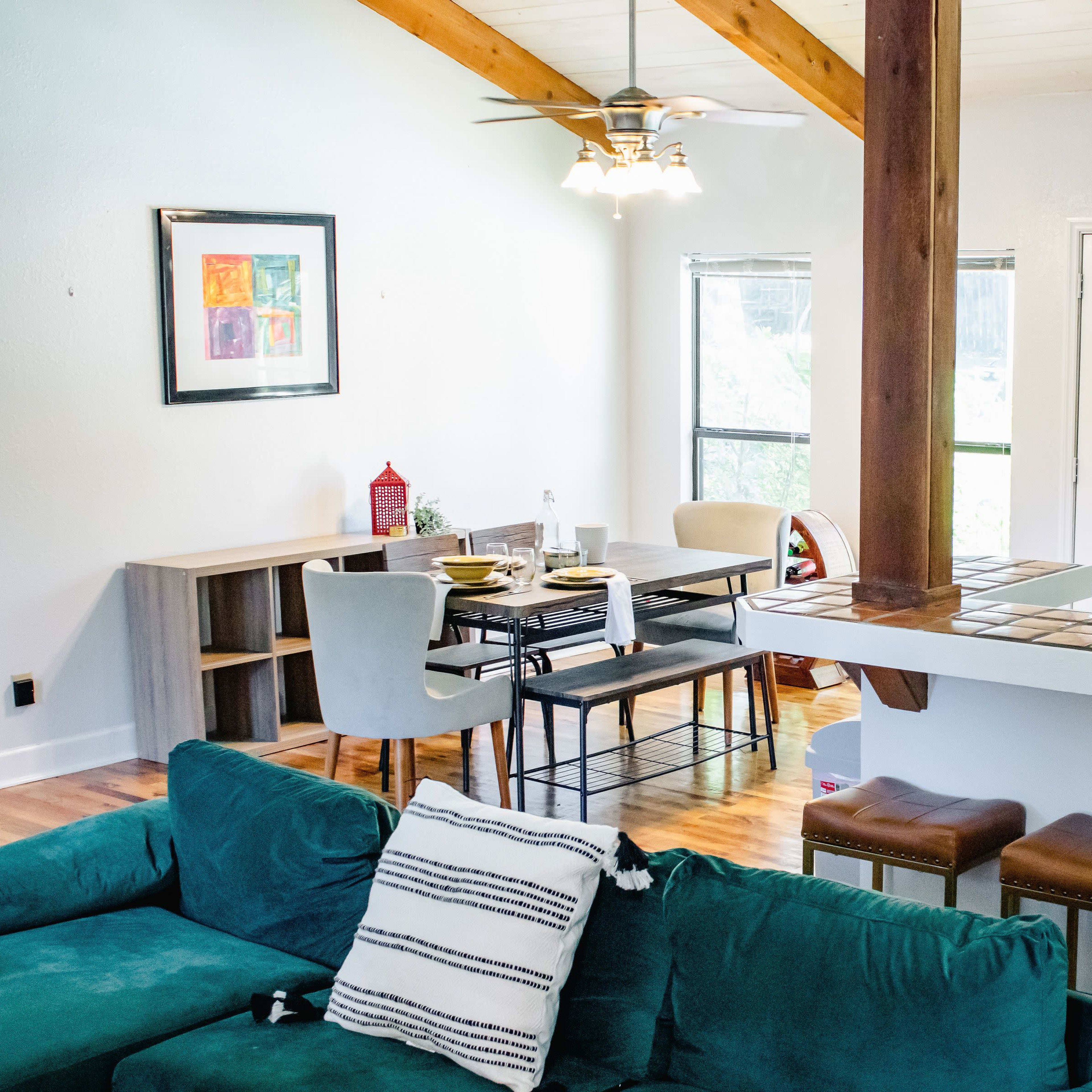 A bright, open-concept living area with a kitchen, dining table, and a seating area featuring a green couch.