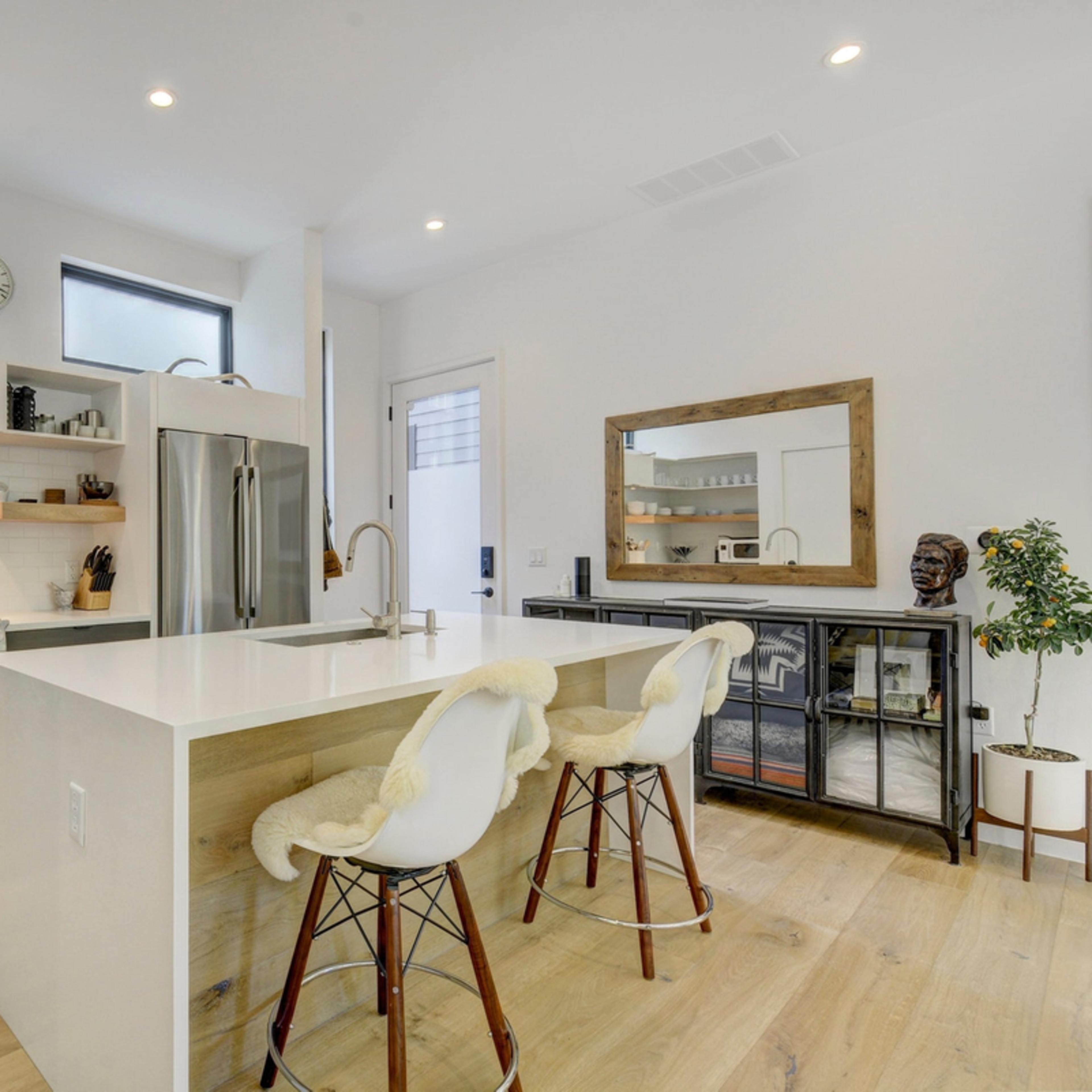 A modern kitchen features a central island with bar stools, sleek cabinetry, stainless steel appliances, and open shelving.