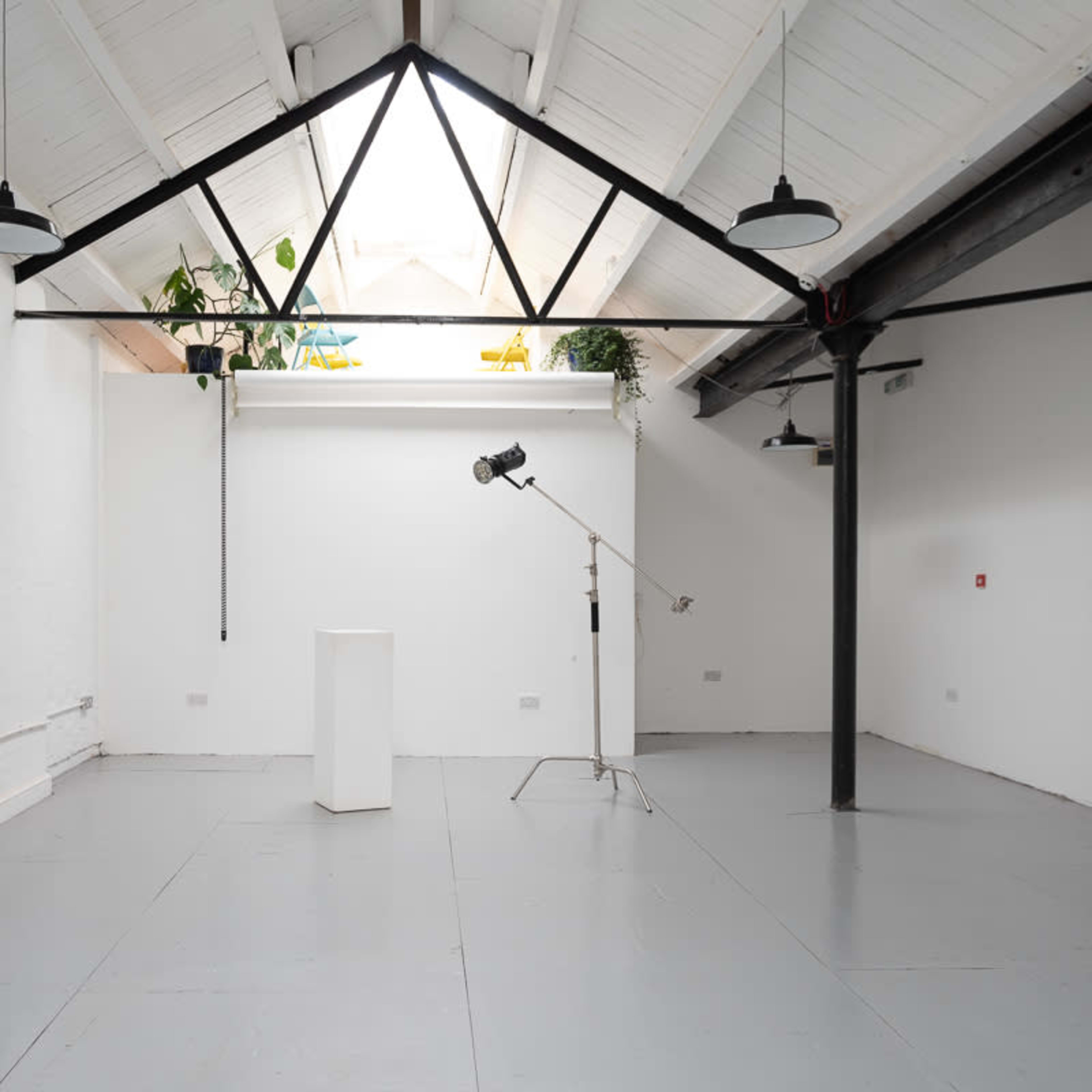 A spacious, empty room with white walls, a high vaulted ceiling, and a pedestal under a lighting setup.